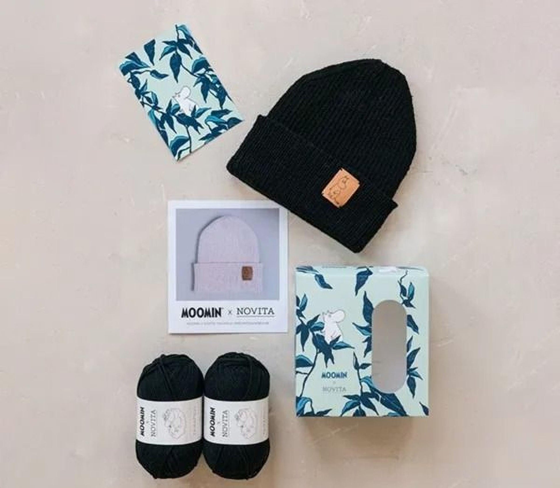 various items related to knitting and crochet, including a black knit cap, two balls of yarn, a box, and a card with a leaf pattern.
