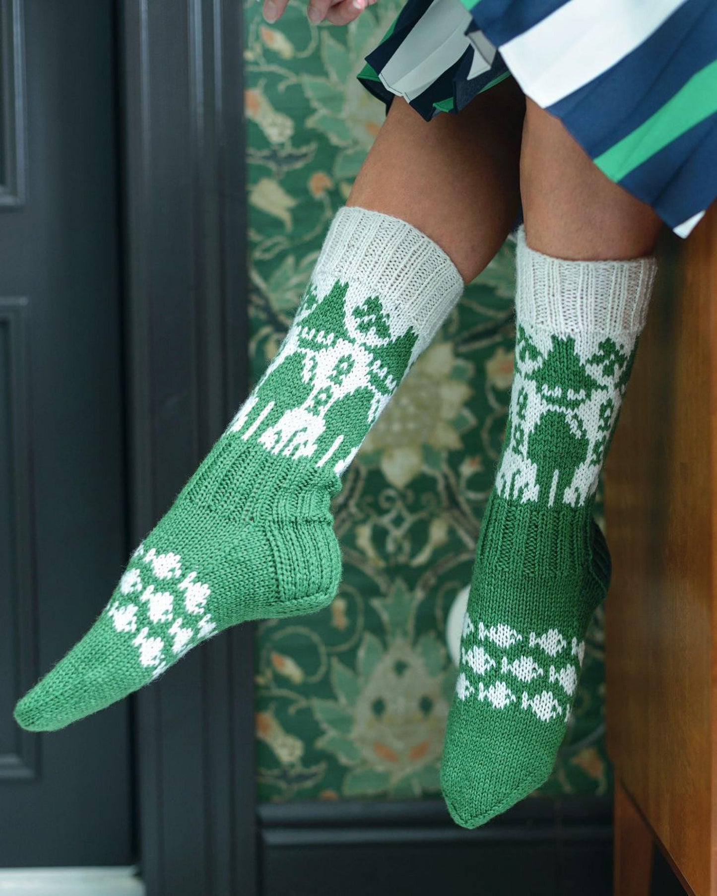 A pair of green and white knitted socks with a pattern of trees and snowflakes.