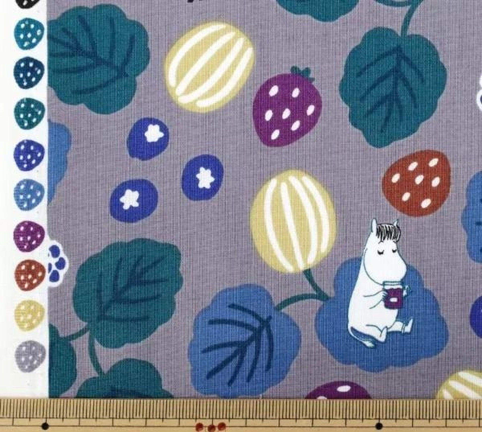a fabric with a playful and whimsical design, including various fruits and leaves in different colors. A small white character resembling a character from a children's book is also present in the image.
