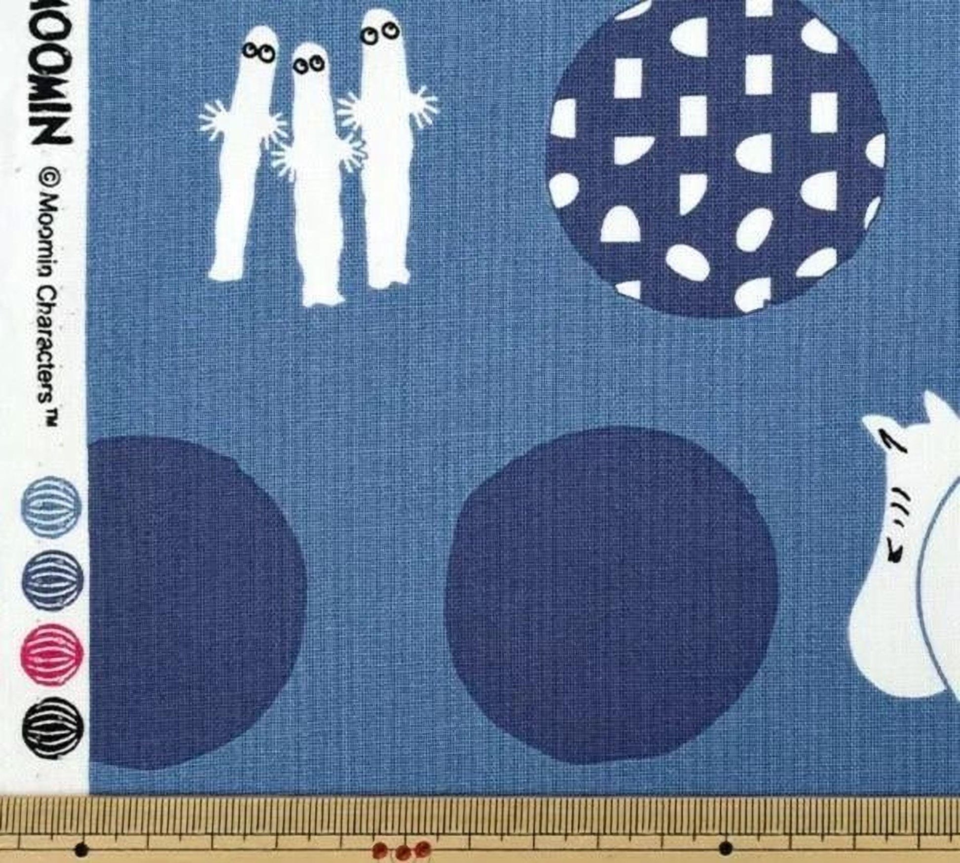 The image is a fabric with a blue background and various abstract shapes and figures, including three white figures, a blue circle, and a white animal.