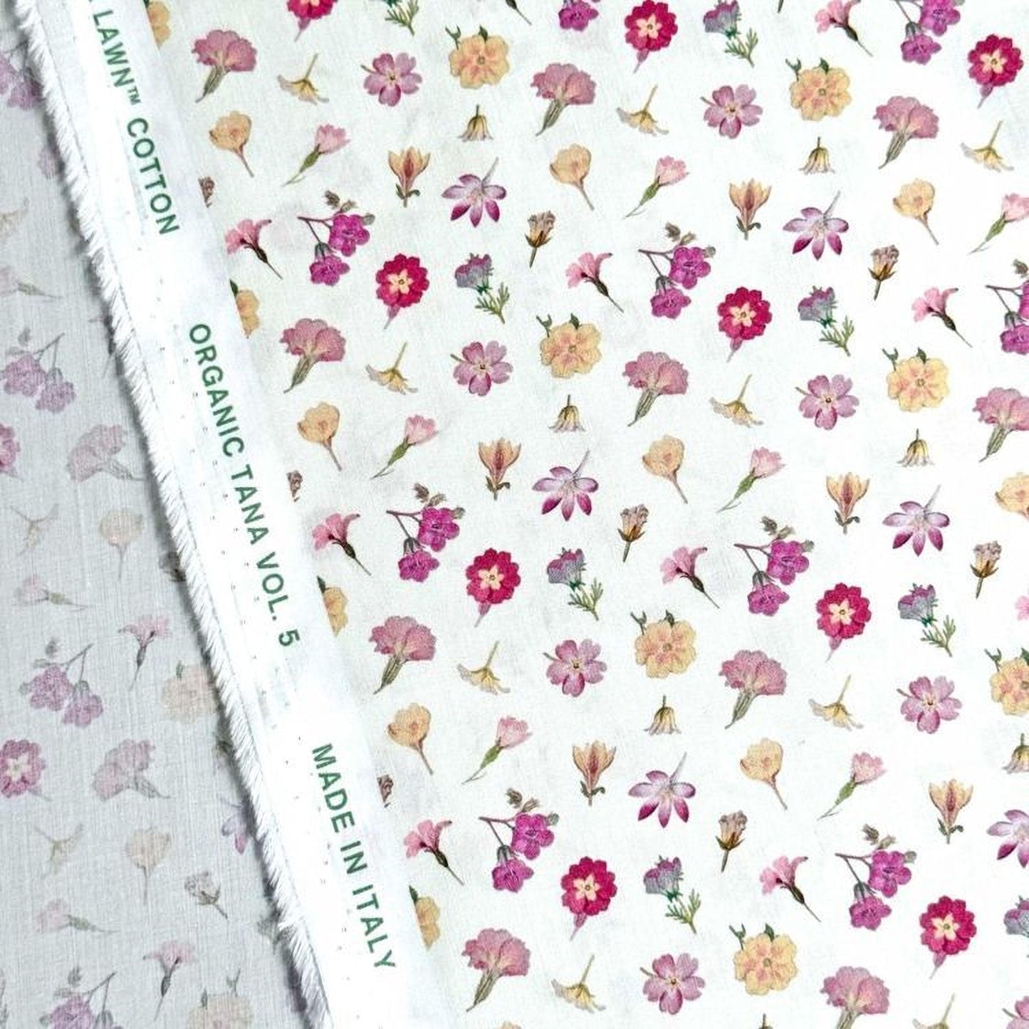 a fabric with a floral pattern, including various types of flowers in different colors such as pink, yellow, and purple. The fabric appears to be made of cotton and is labeled as "Organic Tana Vol. 5" and "Made in Italy".
