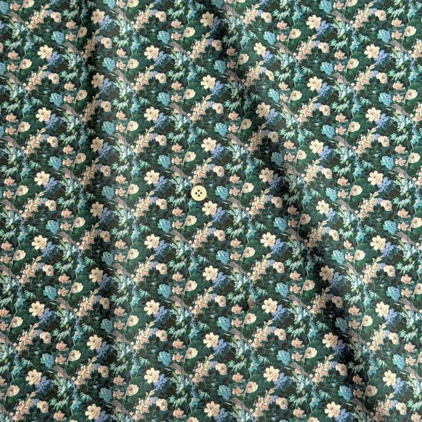 a close-up view of a fabric with a floral pattern. The pattern consists of various shades of green and white flowers, interspersed with small white and beige flowers. The fabric appears to be made of a soft, textured material, and there is a small white button visible in the center of the pattern.