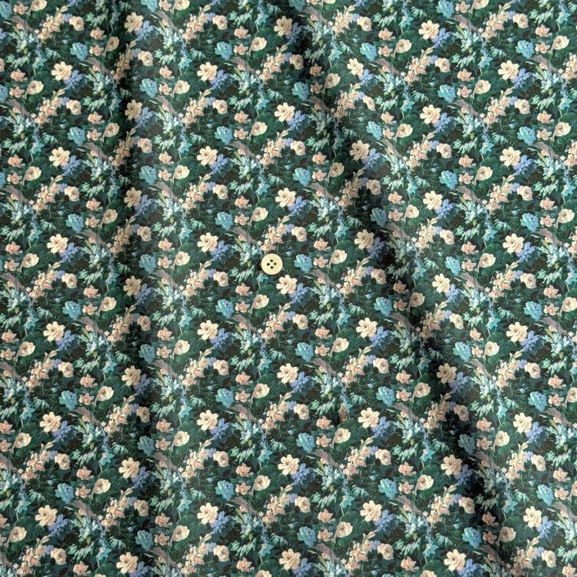 a close-up view of a fabric with a floral pattern. The pattern consists of various shades of green and white flowers, interspersed with small white and beige flowers. The fabric appears to be made of a soft, textured material, and there is a small white button visible in the center of the pattern.
