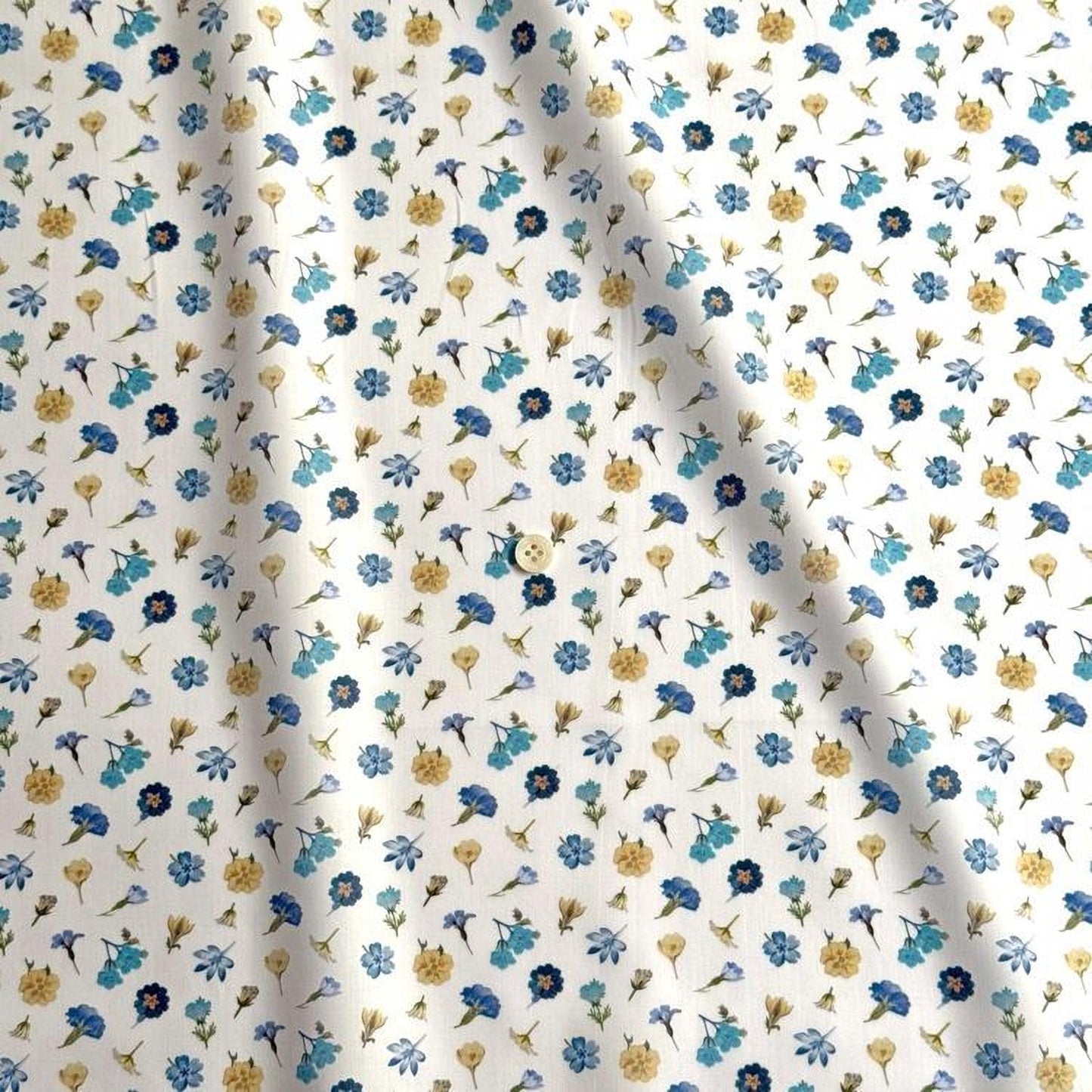 a white fabric with a repeating pattern of blue and yellow flowers. The pattern consists of various types of flowers, including daisies, sunflowers, and other colorful blooms, all arranged in a visually appealing manner. The fabric appears to be made of a soft, flowy material, suitable for clothing or home decor.