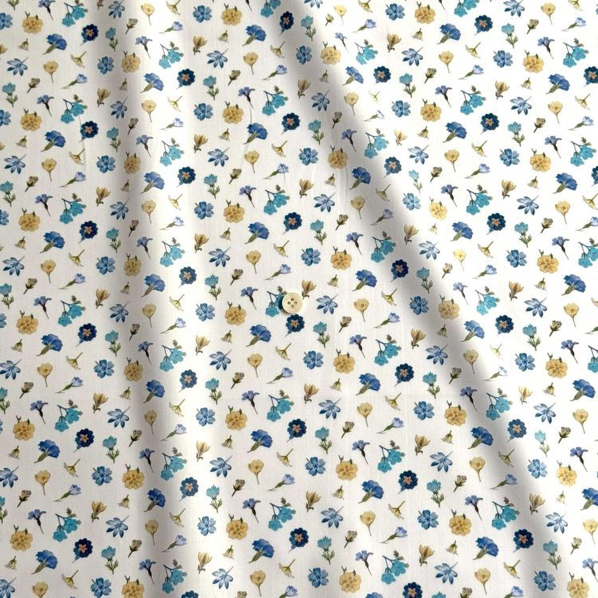 a white fabric with a repeating pattern of blue and yellow flowers. The pattern consists of various types of flowers, including daisies, sunflowers, and other colorful blooms, all arranged in a visually appealing manner. The fabric appears to be made of a soft, flowy material, suitable for clothing or home decor.