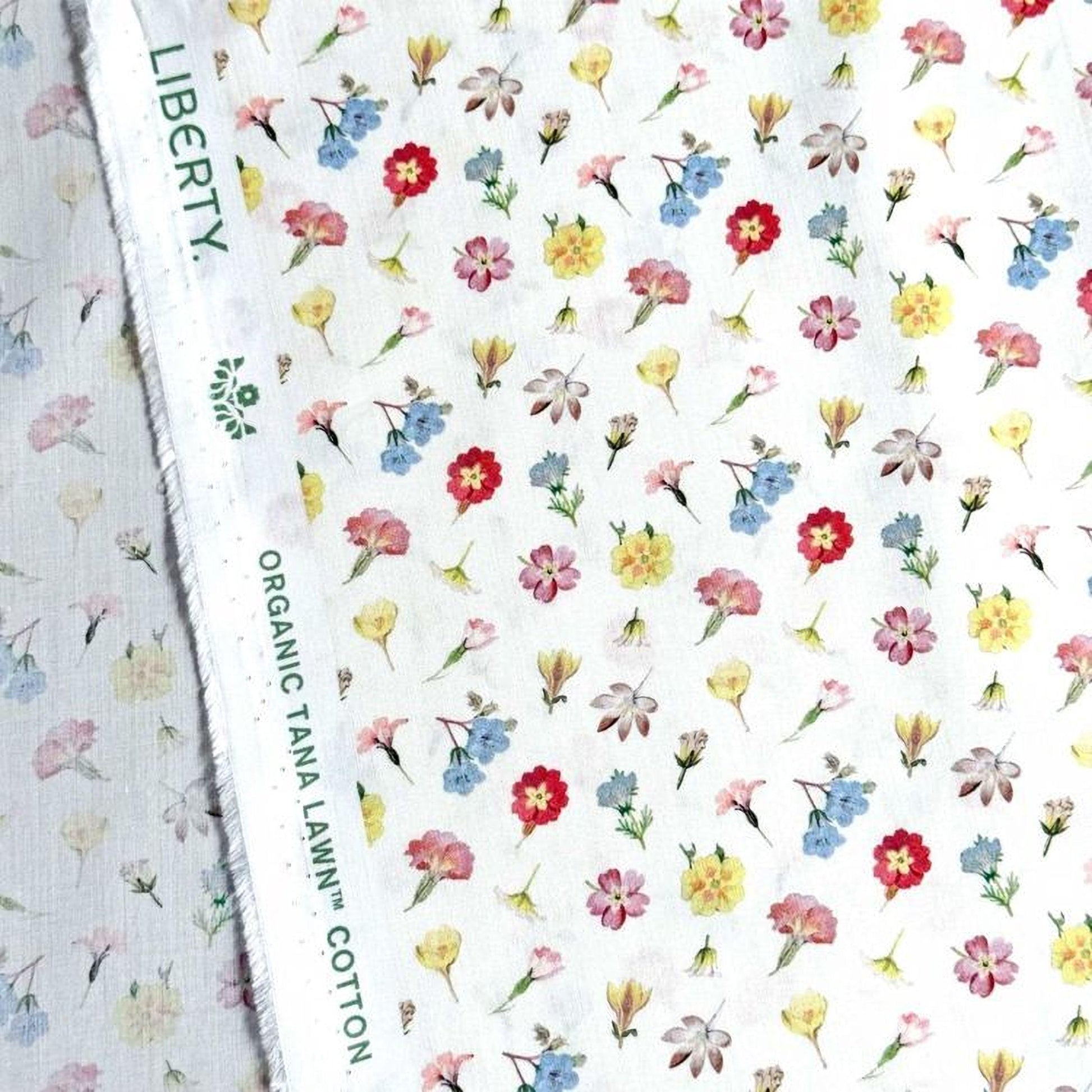 a close-up view of a fabric with a repeating floral pattern. The pattern consists of various types of flowers, including daisies, roses, and other colorful blooms, arranged in a visually appealing manner. The fabric appears to be made of cotton and is likely used for clothing or home decor items.