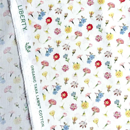 a close-up view of a fabric with a repeating floral pattern. The pattern consists of various types of flowers, including daisies, roses, and other colorful blooms, arranged in a visually appealing manner. The fabric appears to be made of cotton and is likely used for clothing or home decor items.