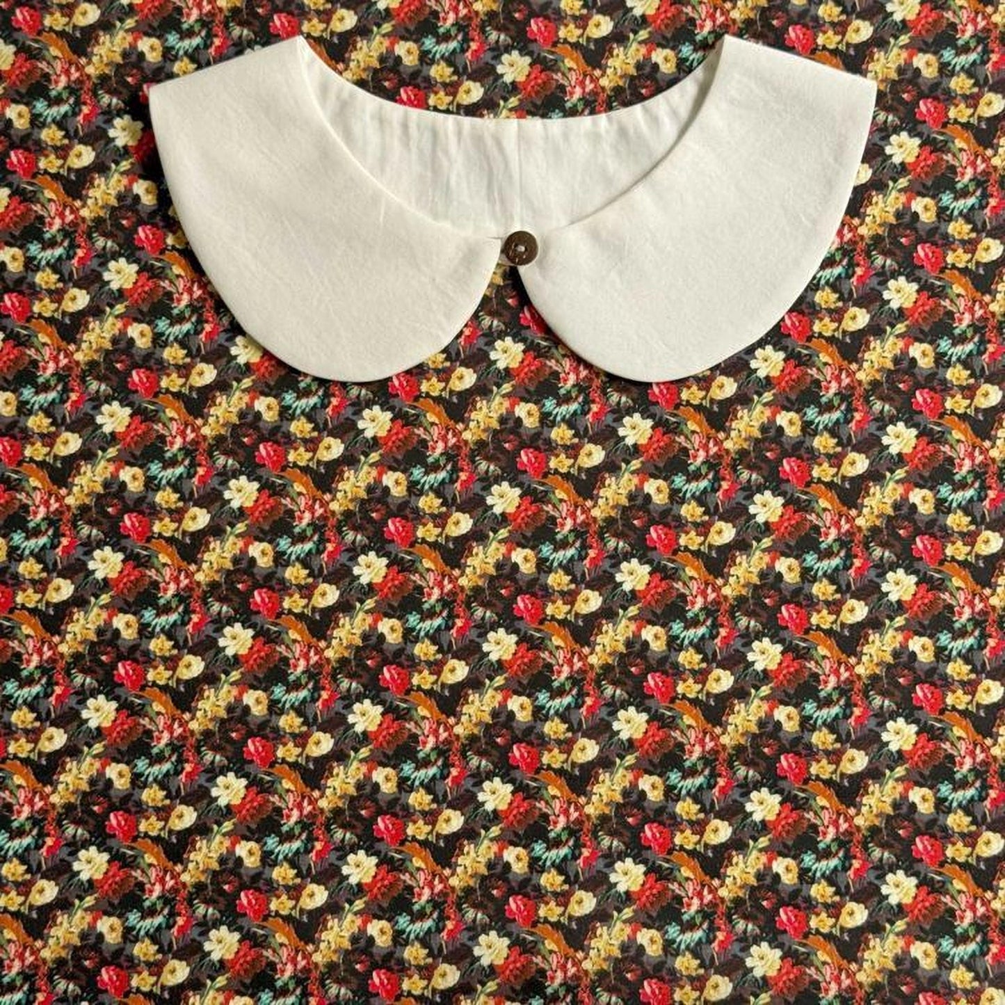 a white collar with a button, set against a background of a colorful floral print.