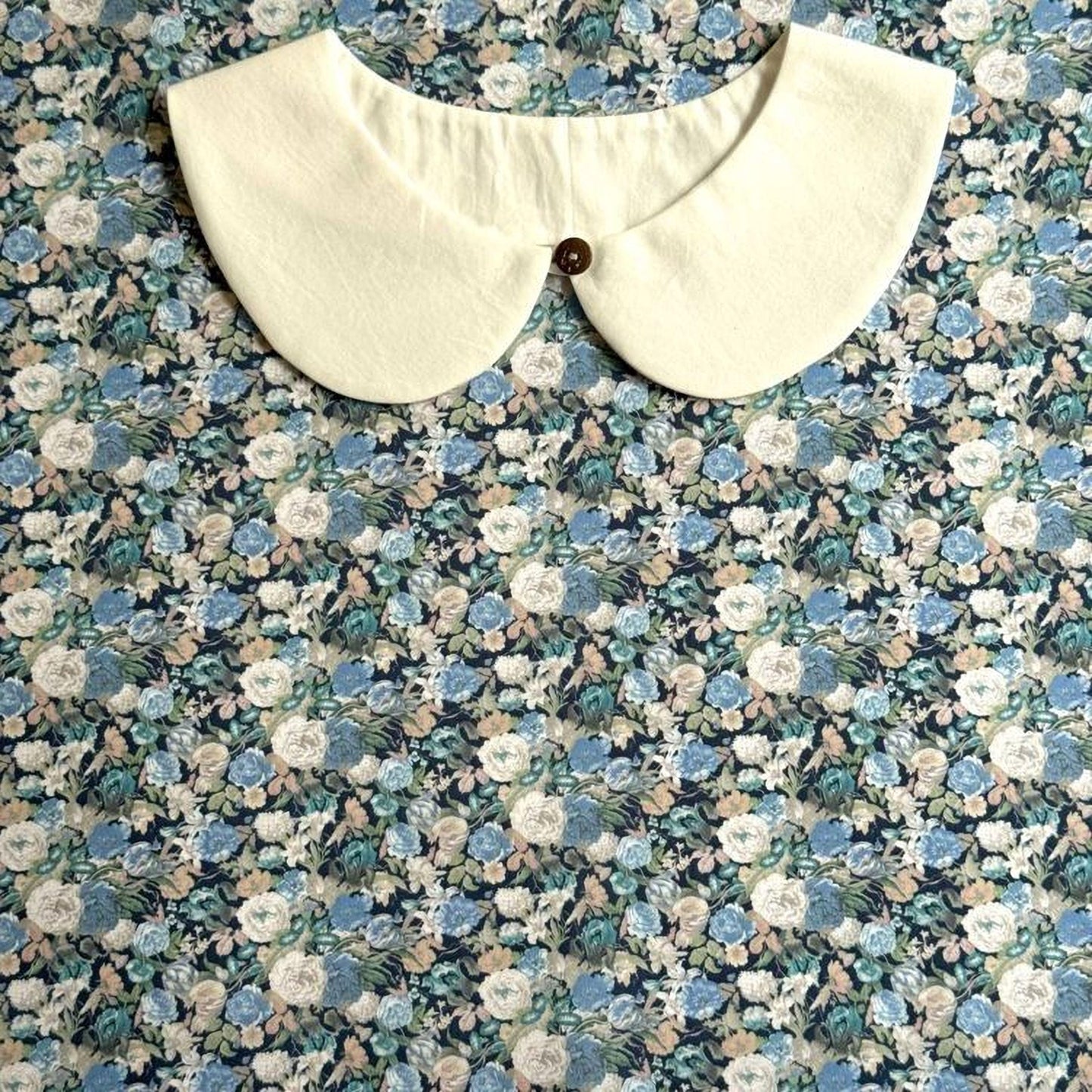 A white collar with a button is displayed against a background of a floral print fabric.