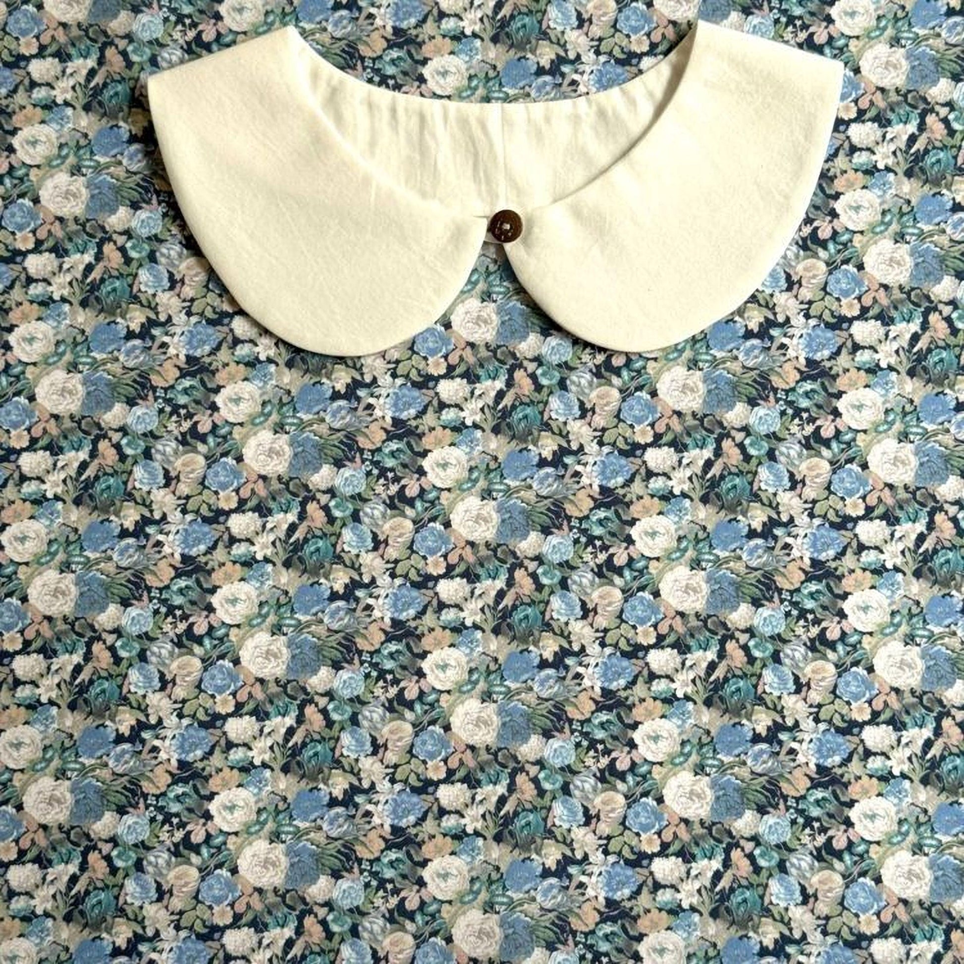 A white collar with a button is displayed against a background of a floral print fabric.