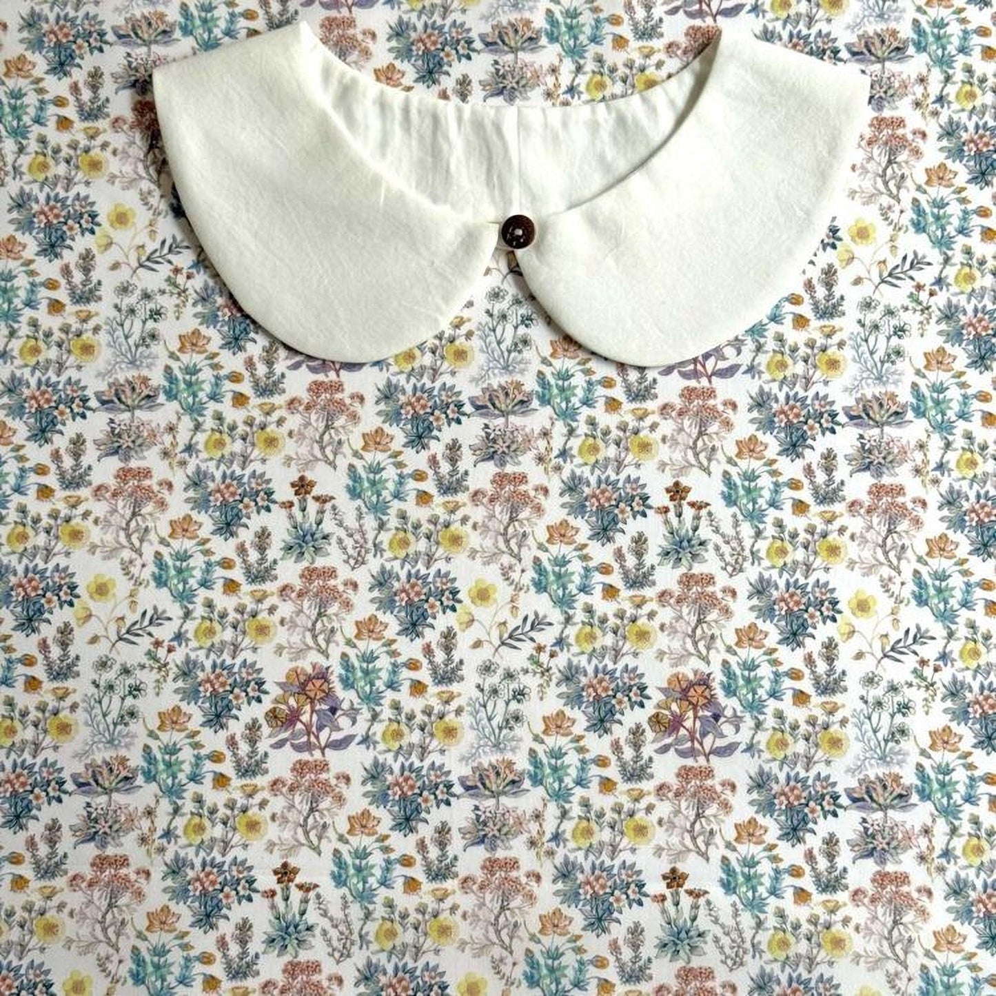 a white collar with a button, placed on a floral print background.
