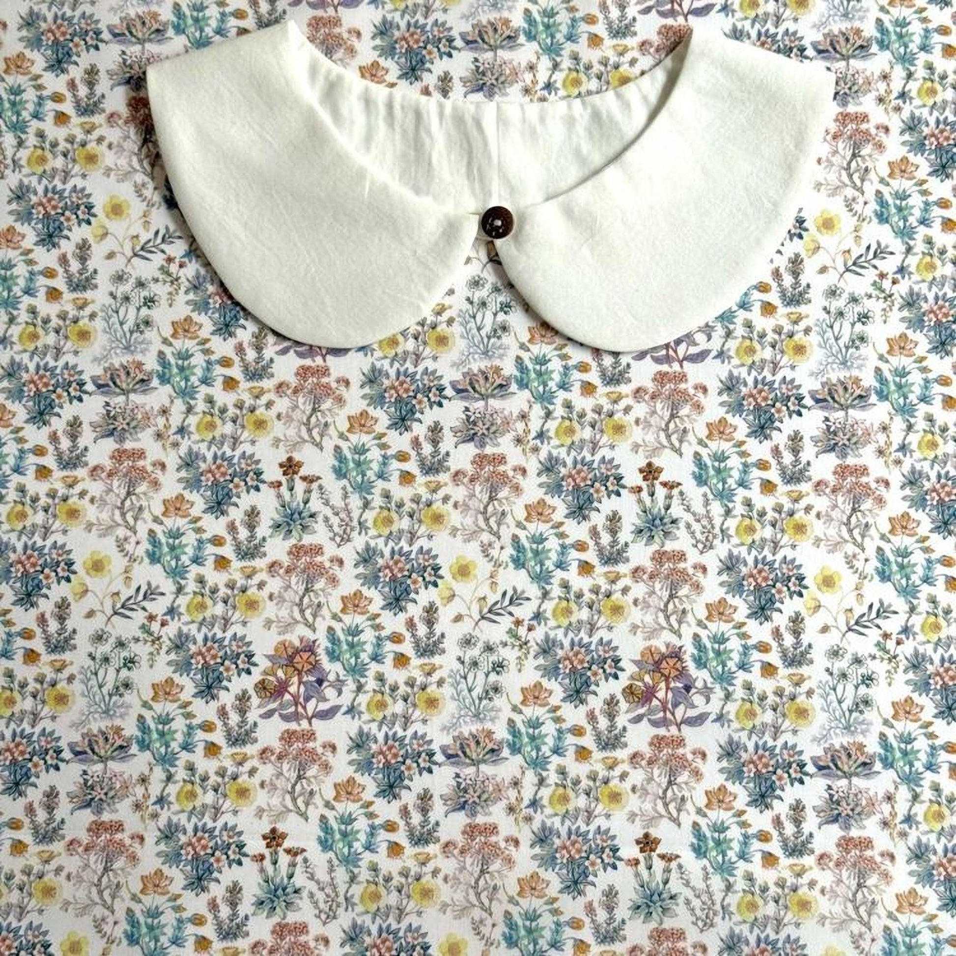 a white collar with a button, placed on a floral print background.