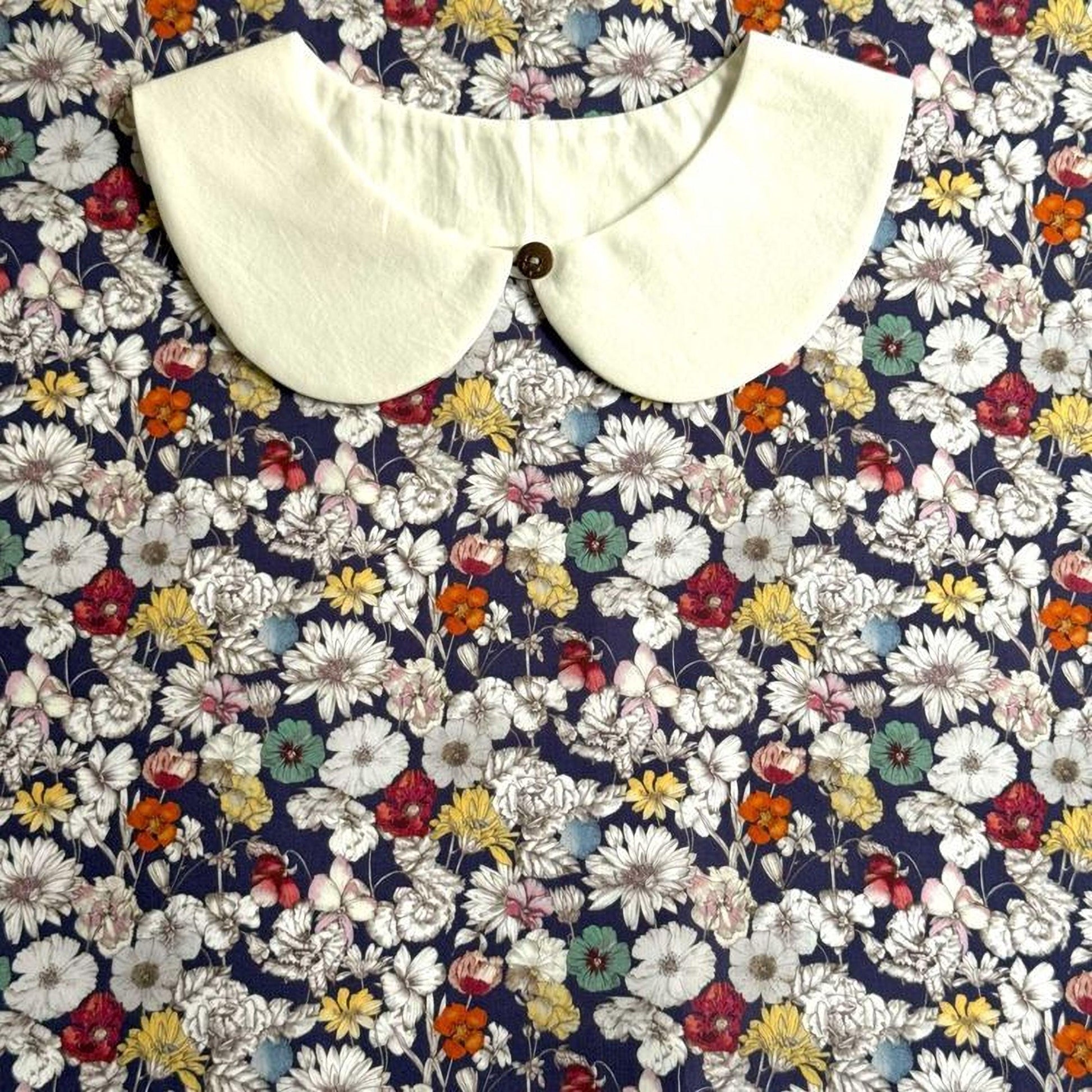 a white collar with a button, set against a background of a floral print with various colors and patterns.