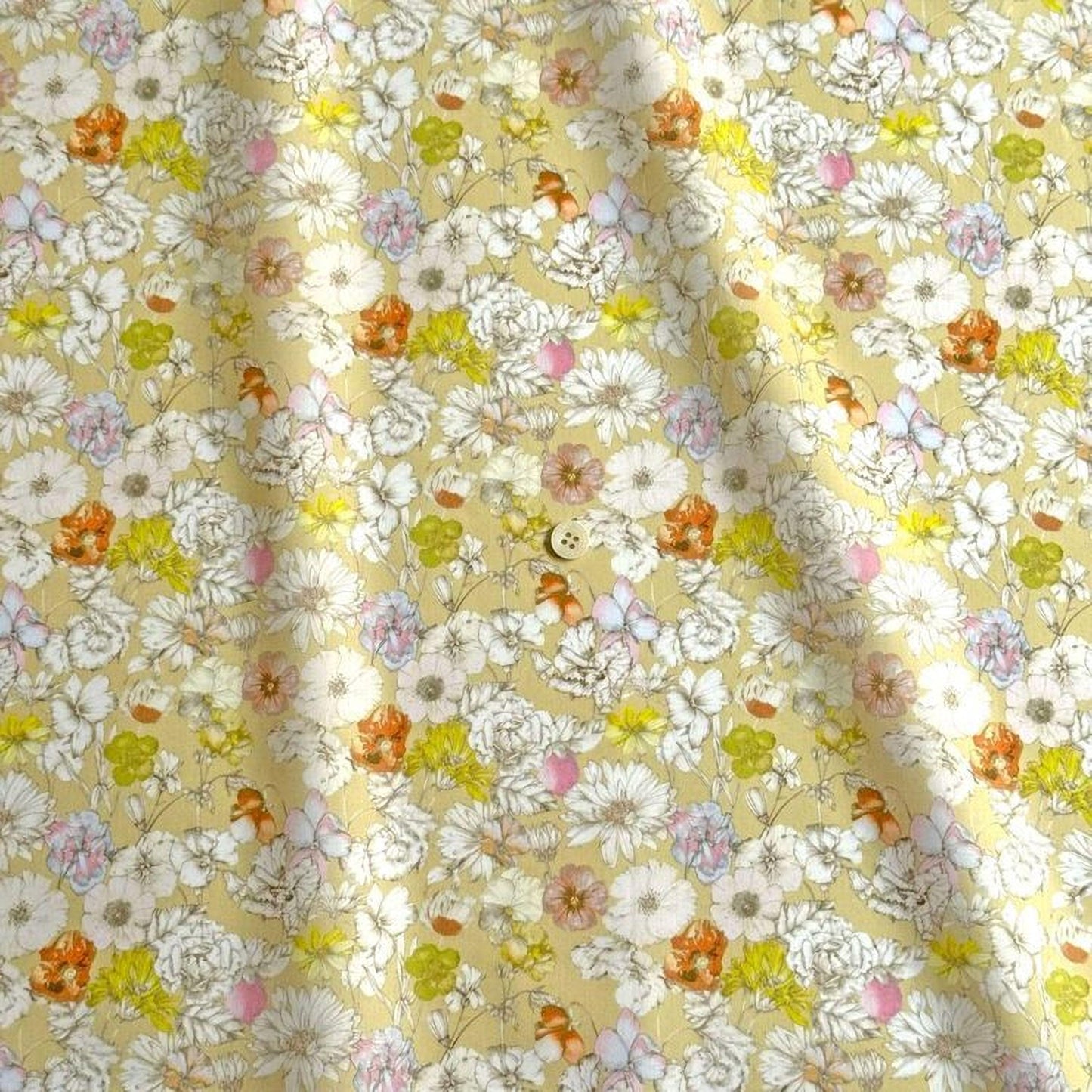 a close-up view of a fabric with a floral pattern. The fabric appears to be a light yellow color, and it is adorned with a variety of colorful flowers in shades of white, orange, and pink. The flowers are scattered throughout the fabric, creating a vibrant and lively visual effect. The fabric is folded and crumpled, giving it a textured appearance.