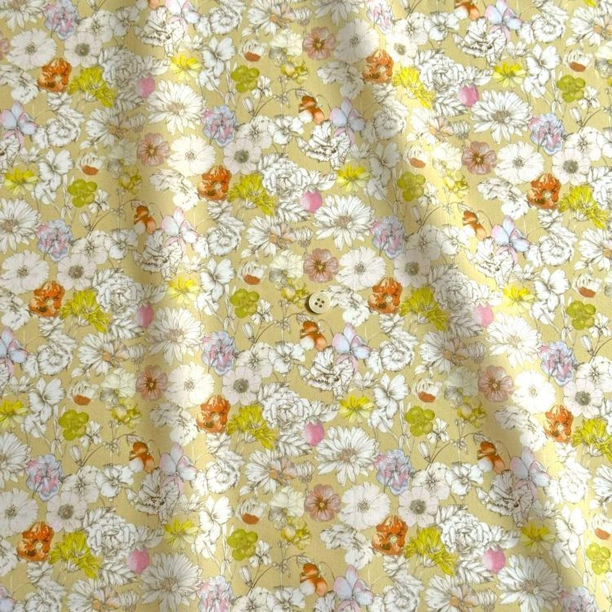 a close-up view of a fabric with a floral pattern. The fabric appears to be a light yellow color, and it is adorned with a variety of colorful flowers in shades of white, orange, and pink. The flowers are scattered throughout the fabric, creating a vibrant and lively visual effect. The fabric is folded and crumpled, giving it a textured appearance.