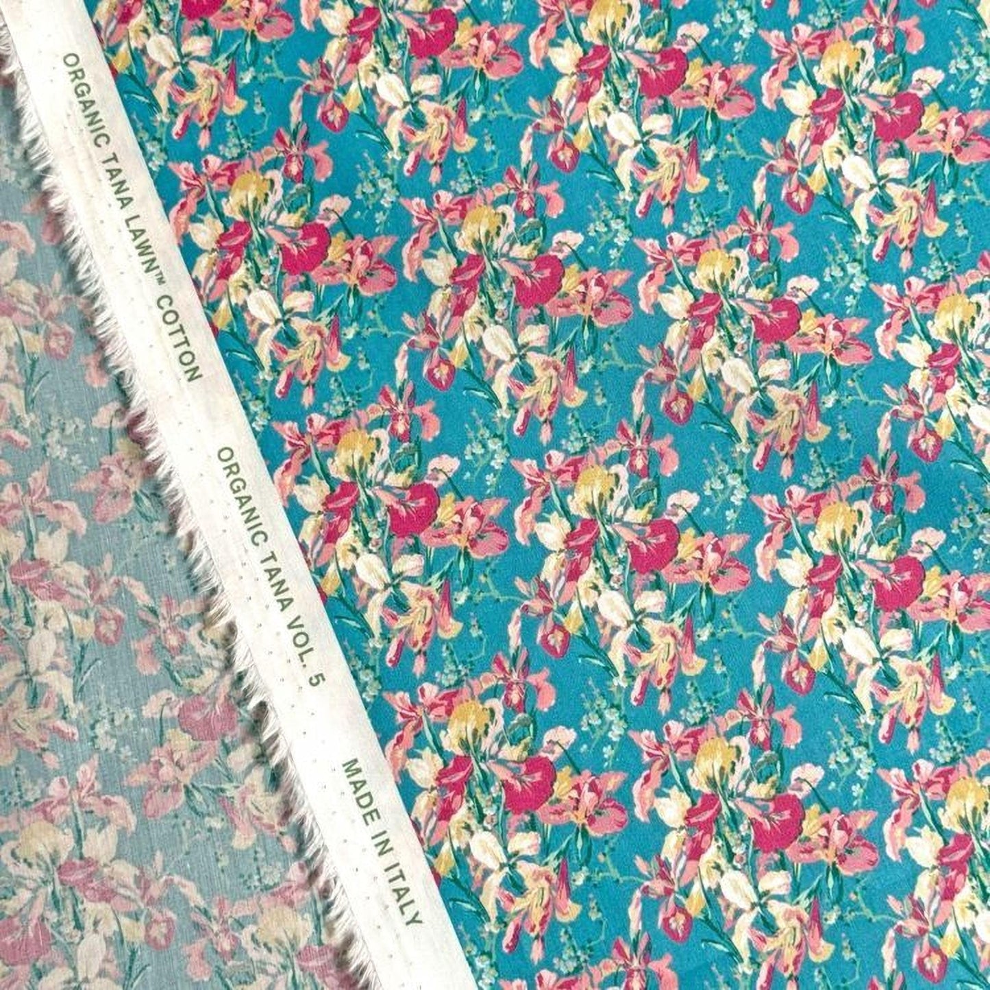 a close-up view of a fabric with a floral pattern in shades of blue and pink. The fabric appears to be made of organic cotton and is displayed on a white fabric with a label that reads "Organic cotton" and "TANA LAWN® VOL. 5".