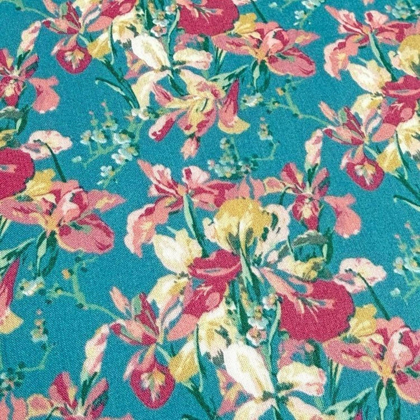a close-up view of a vibrant floral pattern on a teal background. The pattern consists of a variety of colorful flowers, including red, yellow, and pink blooms, arranged in a visually appealing manner. The flowers are depicted in different stages of bloom, creating a dynamic and lively visual effect. The teal background provides a contrasting backdrop that accentuates the vivid colors of the flowers.