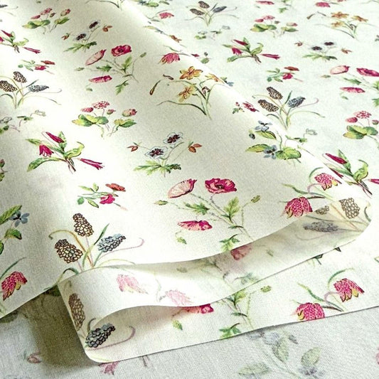 a close-up view of a fabric with a floral pattern, including various types of flowers and leaves. The fabric appears to be white and has a repeating pattern of flowers and leaves throughout its surface.