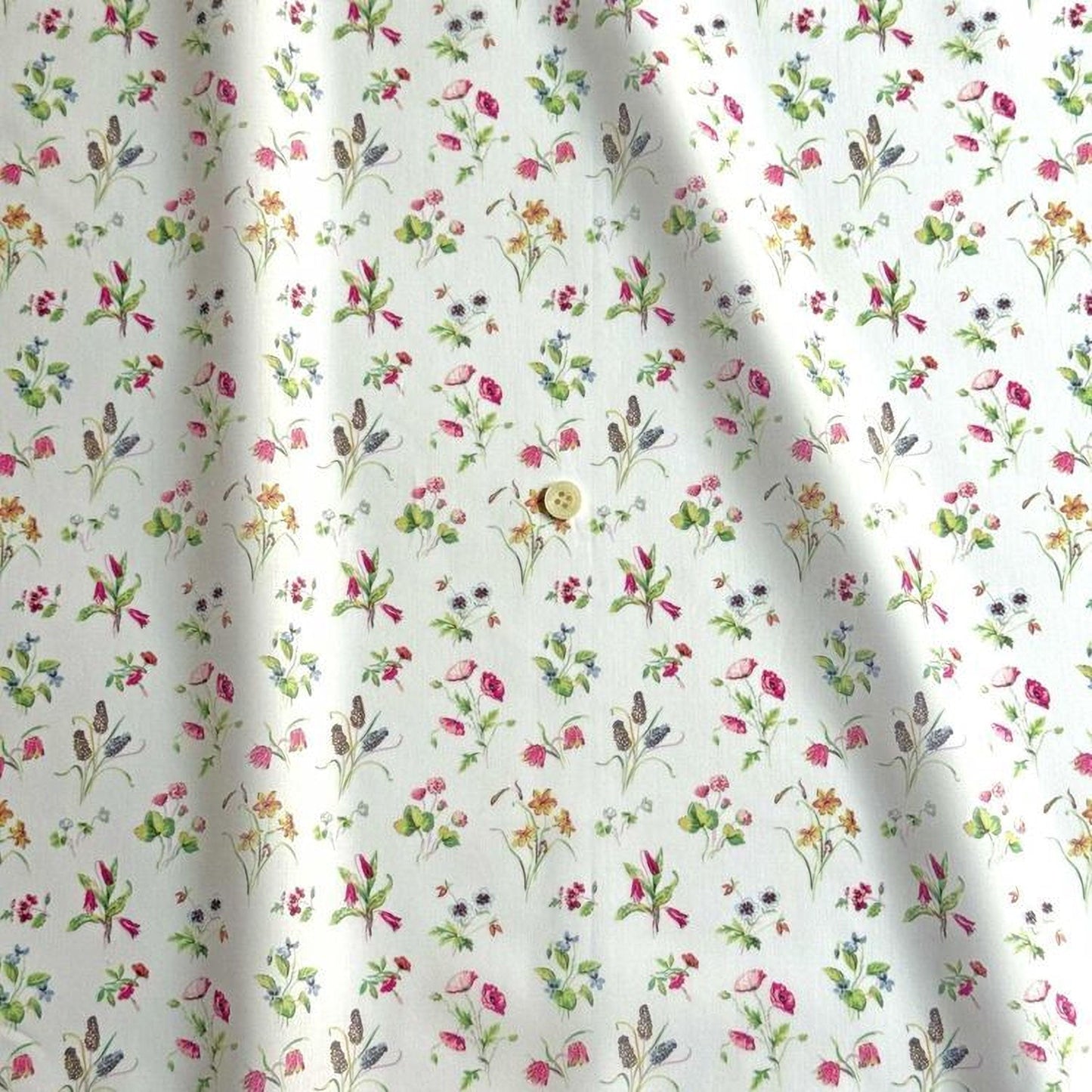 a close-up view of a fabric with a repeating floral pattern in shades of pink, green, and yellow. The pattern is composed of various flowers and leaves, creating a visually appealing and intricate design. The fabric appears to be made of a soft, light-colored material, suitable for clothing or home decor.