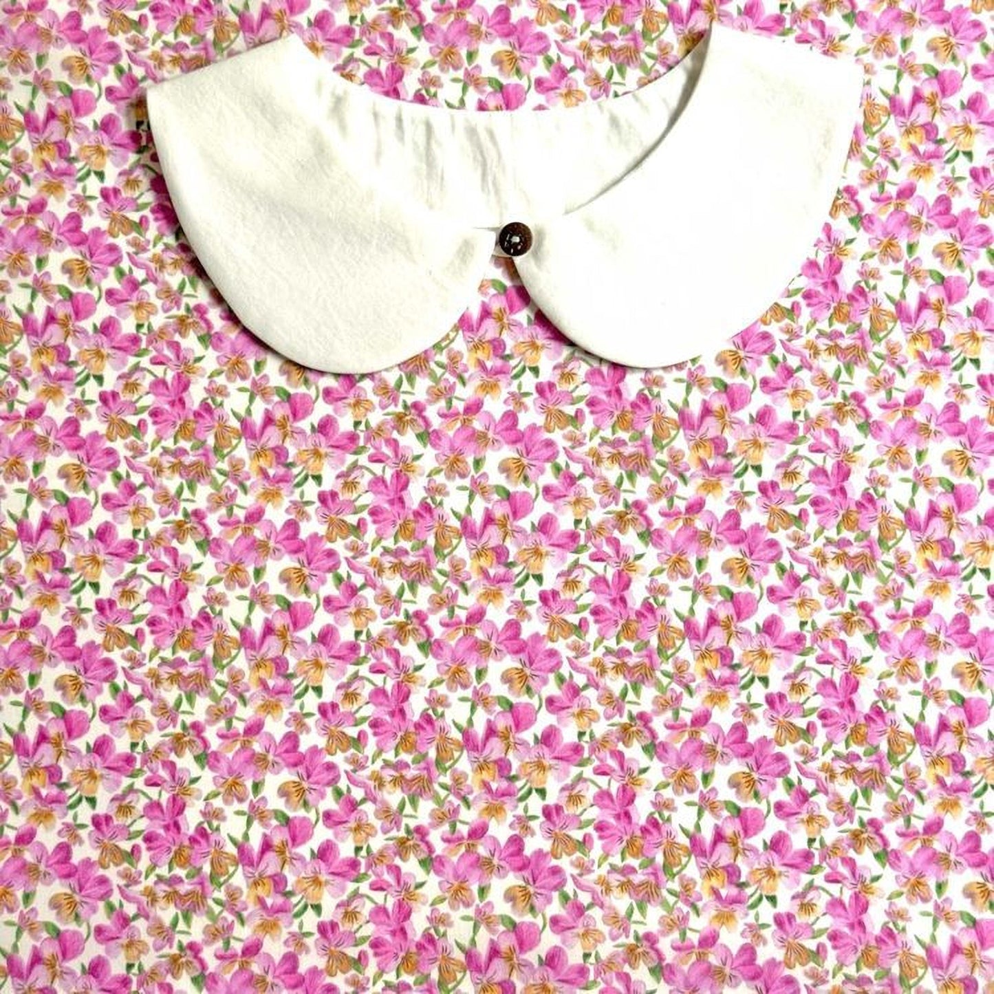 a white collar with a button, set against a background of a floral print with pink and yellow flowers.