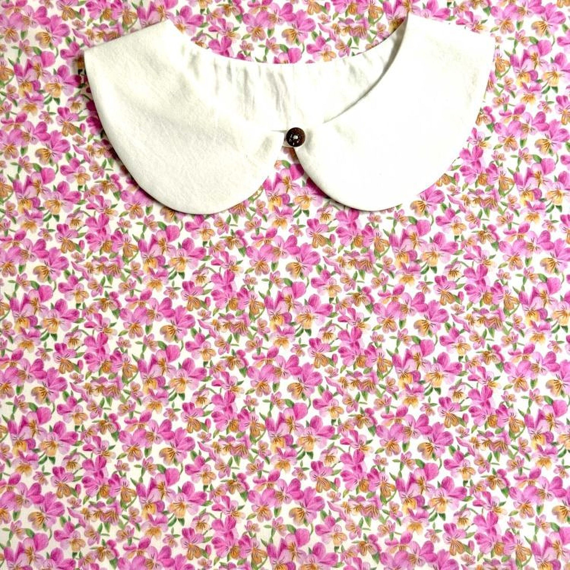 a white collar with a button, set against a background of a floral print with pink and yellow flowers.