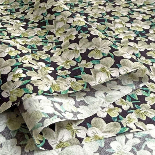 a close-up view of a fabric with a floral pattern in shades of green and white. The fabric appears to be a dark-colored material with a repeating pattern of white flowers and green leaves. The image does not contain any text or other objects, and the focus is solely on the fabric and its floral design.