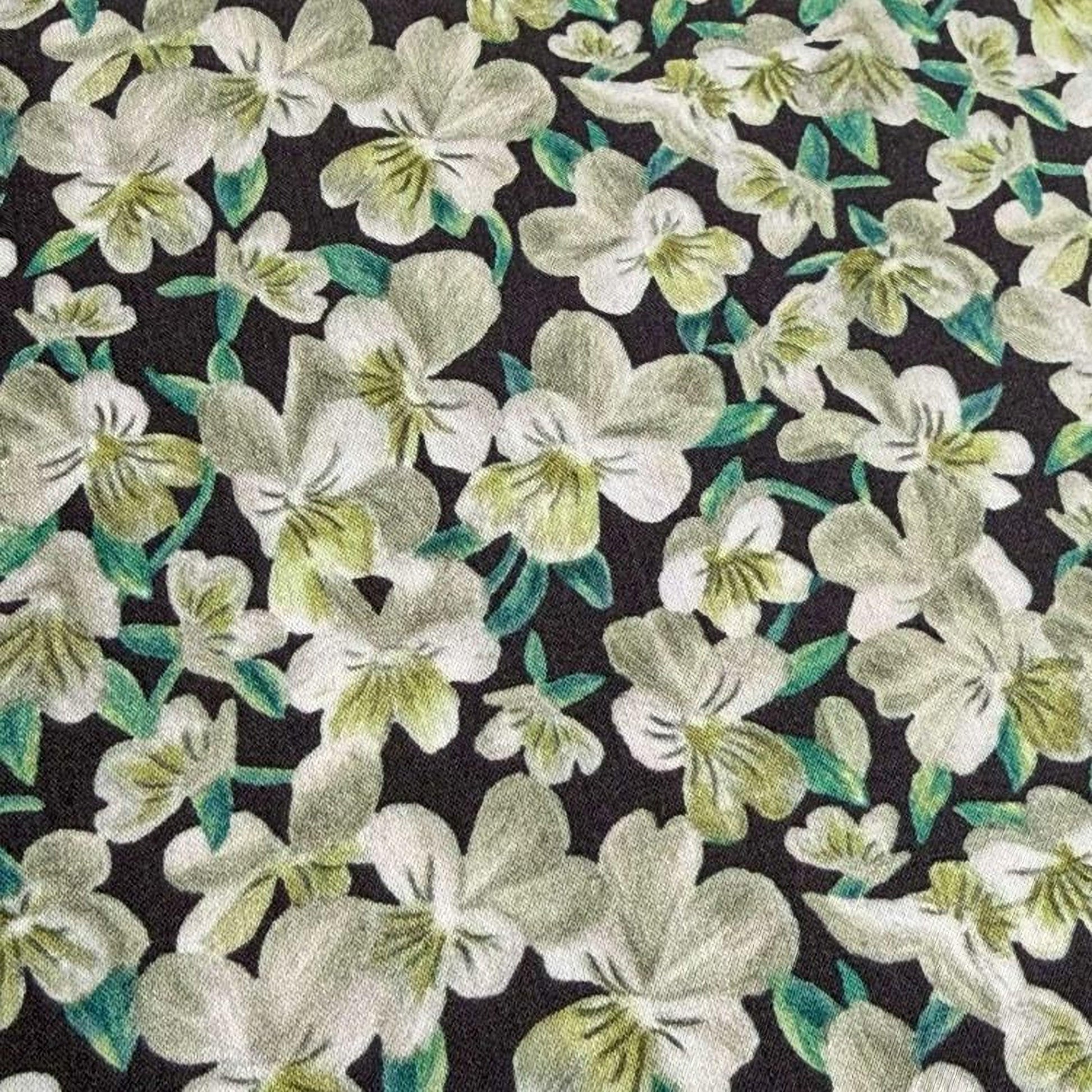 a close-up view of a fabric with a floral pattern. The fabric is predominantly black, with white flowers and green leaves scattered across it. The flowers appear to be in various stages of bloom, creating a dynamic and visually appealing design. The image does not contain any text or other discernible objects, and the focus is solely on the floral pattern on the fabric.