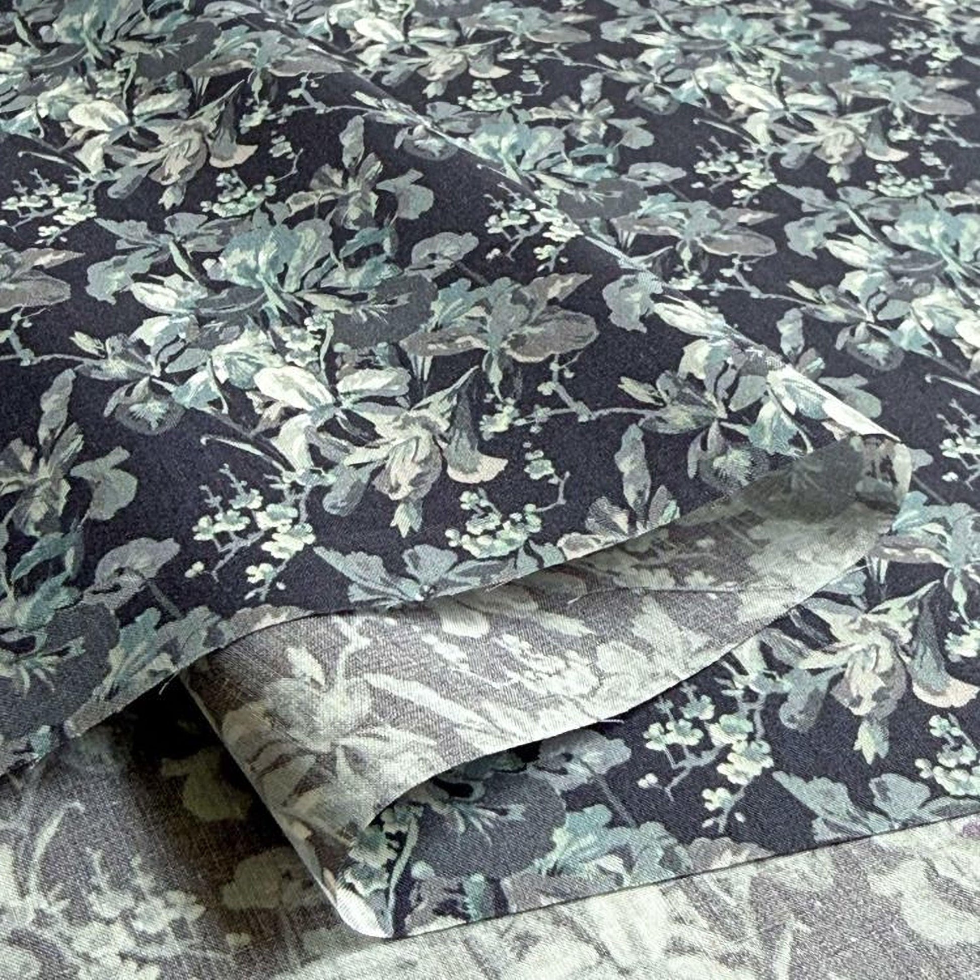 a close-up view of a fabric with a floral pattern in shades of blue and gray. The fabric appears to be folded or rolled, revealing the intricate design of the floral pattern.