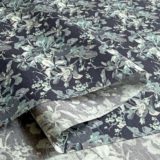 a close-up view of a fabric with a floral pattern in shades of blue and gray. The fabric appears to be folded or rolled, revealing the intricate design of the floral pattern.
