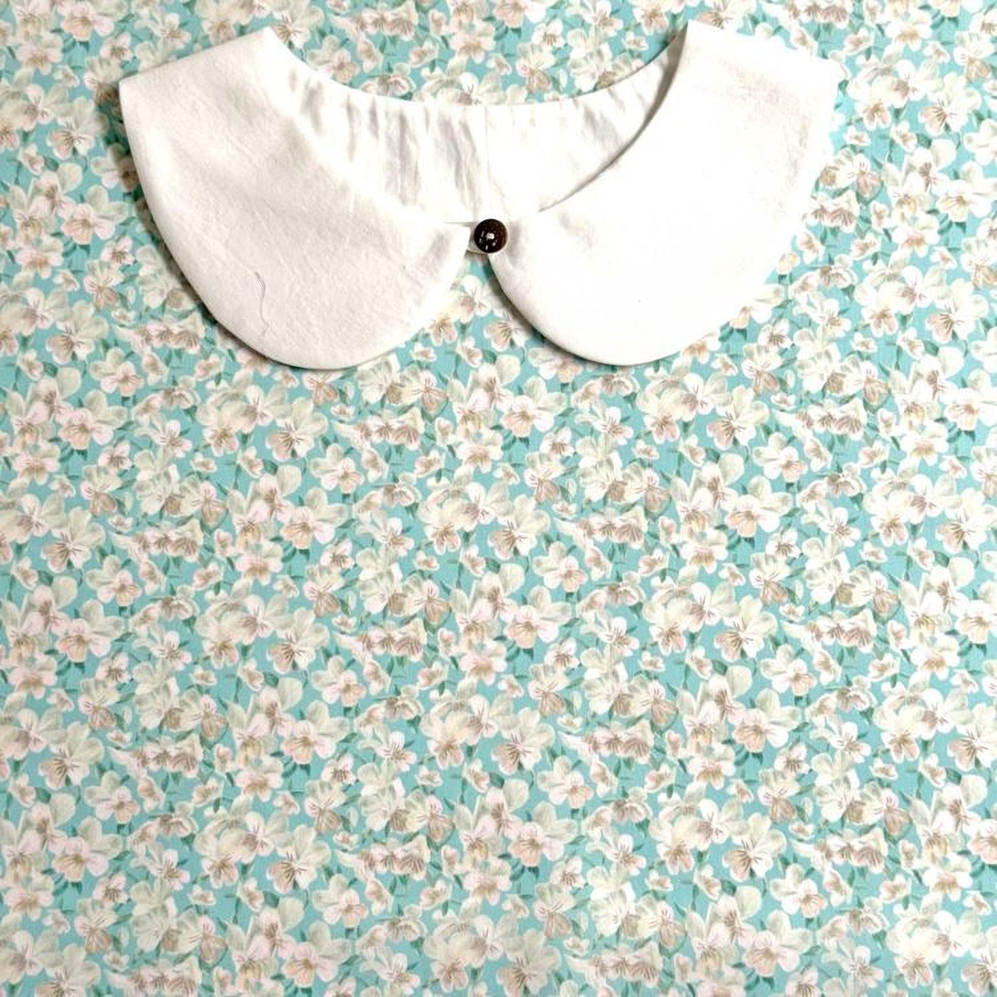 A white collar with a button is displayed against a background of a floral print fabric.