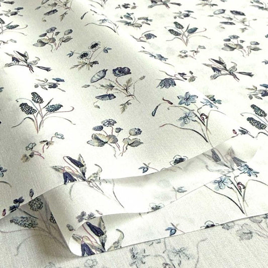 a close-up view of a fabric with a floral pattern, including various types of flowers and leaves in shades of blue, green, and white.