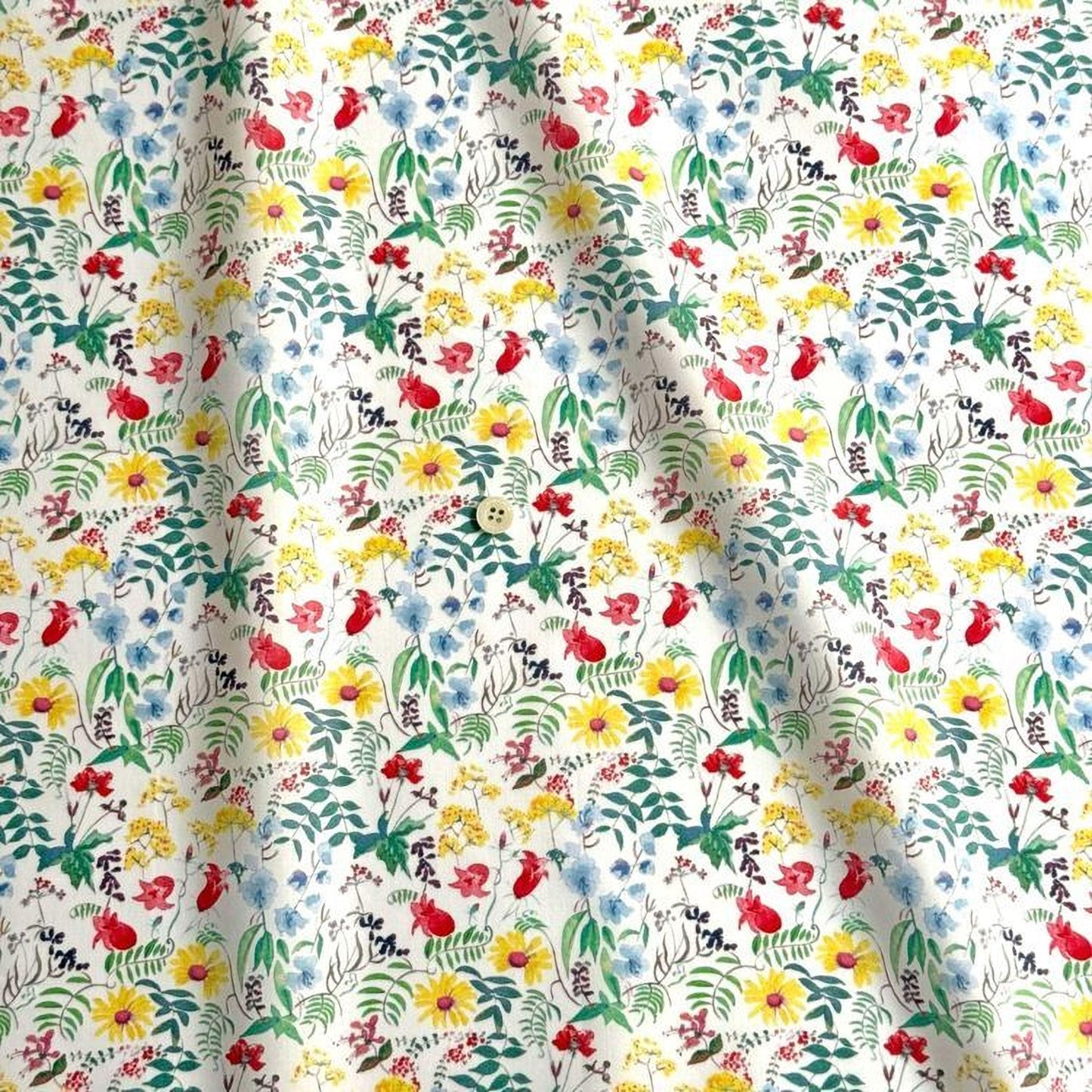 The image is a close-up of a fabric with a vibrant floral pattern. The pattern consists of various flowers and leaves in different colors, including red, yellow, green, and blue. The fabric appears to be made of a soft, white material, and the pattern is intricate and detailed.