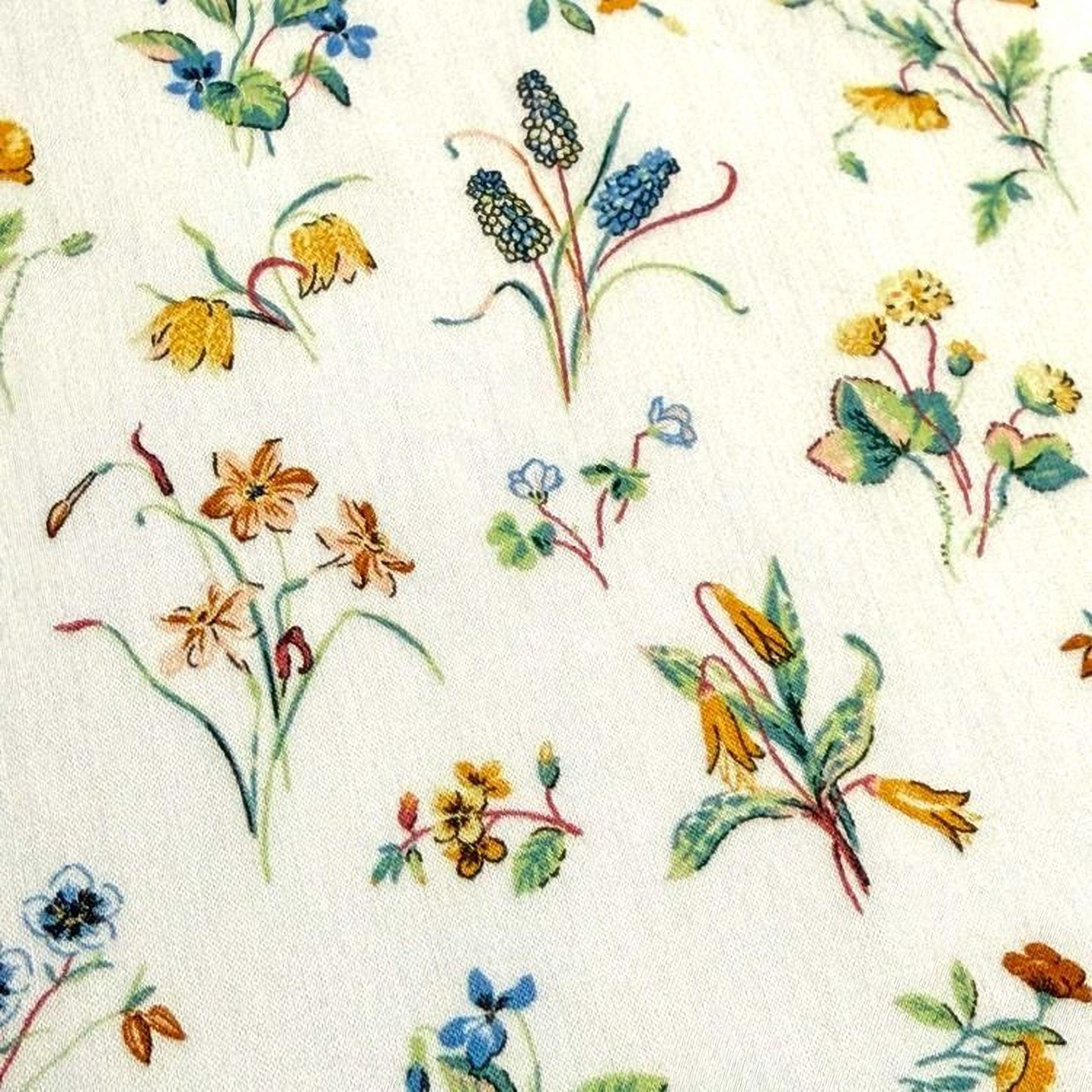 a close-up view of a white fabric adorned with a variety of colorful floral designs, including yellow, orange, blue, and green flowers.