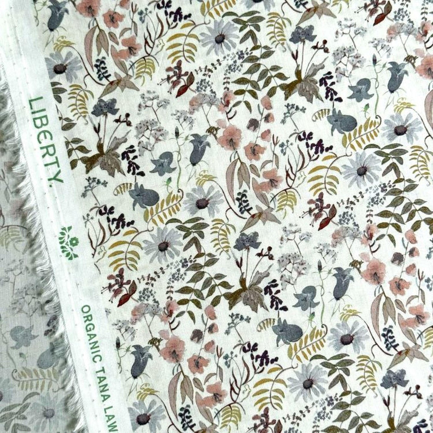 a close-up view of a fabric with a floral pattern. The fabric appears to be a white material with a variety of colorful flowers and leaves printed on it. The pattern is intricate and detailed, showcasing the craftsmanship of the fabric.