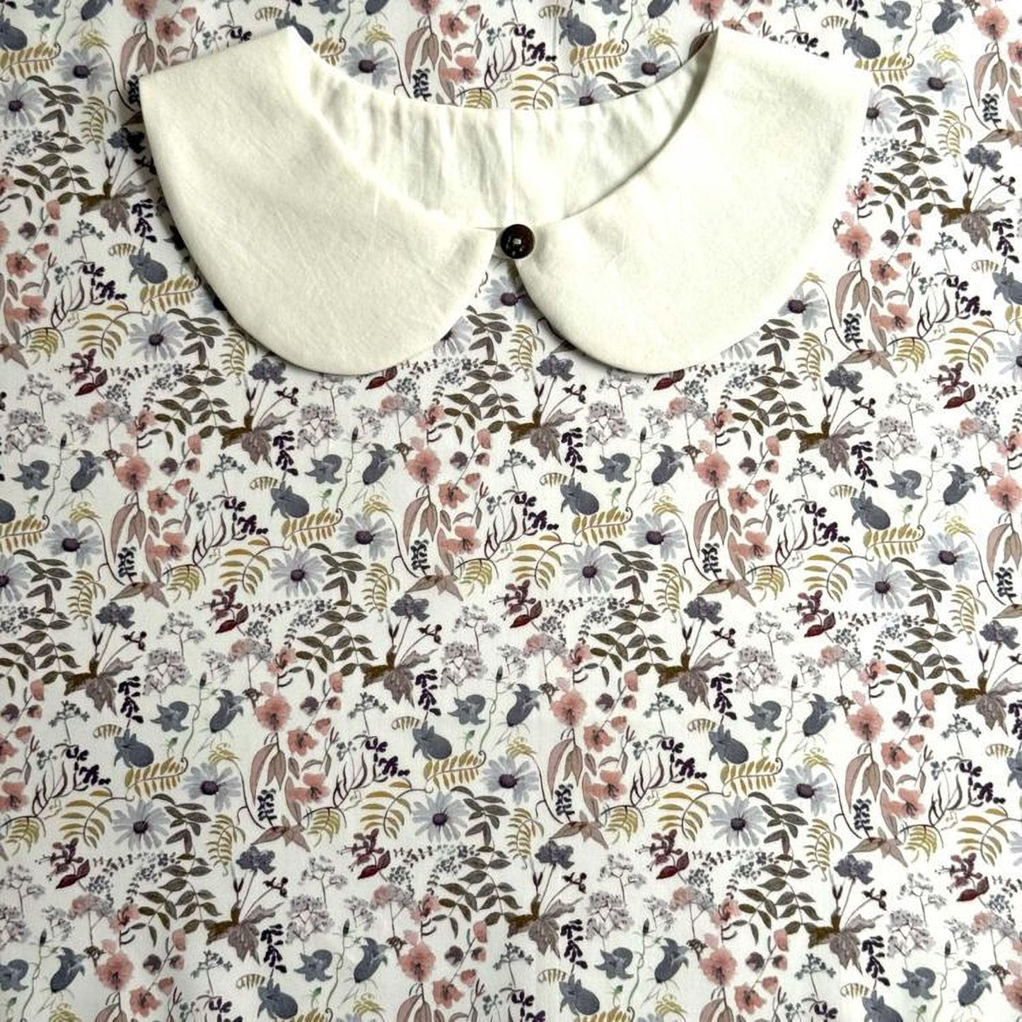 a white collar with a button, placed on a floral print fabric.