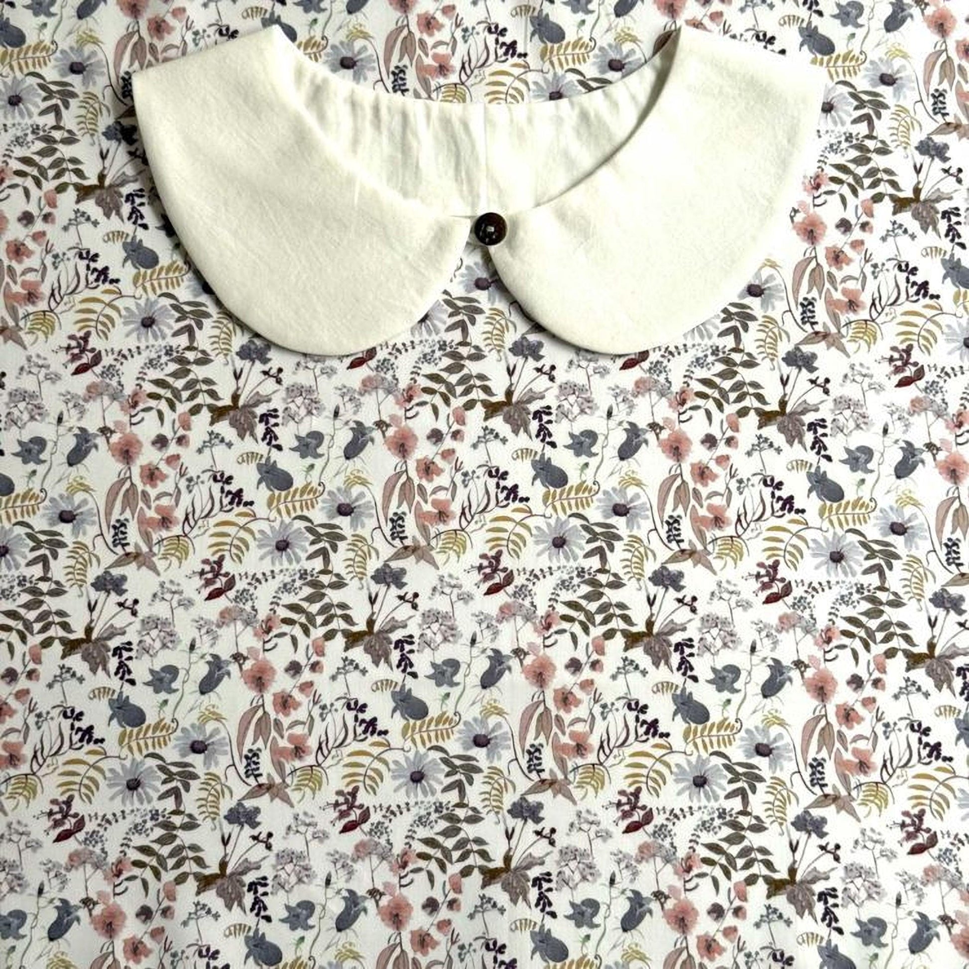 a white collar with a button, placed on a floral print fabric.