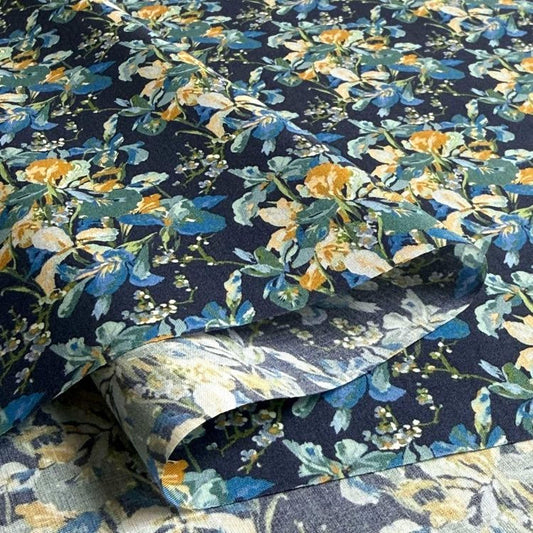 a close-up view of a fabric with a vibrant floral pattern in shades of blue, yellow, and green. The pattern is intricate and detailed, with the flowers and leaves filling the entire fabric. The fabric appears to be a piece of clothing or textile, with the floral pattern adding a touch of color and visual interest to the design.