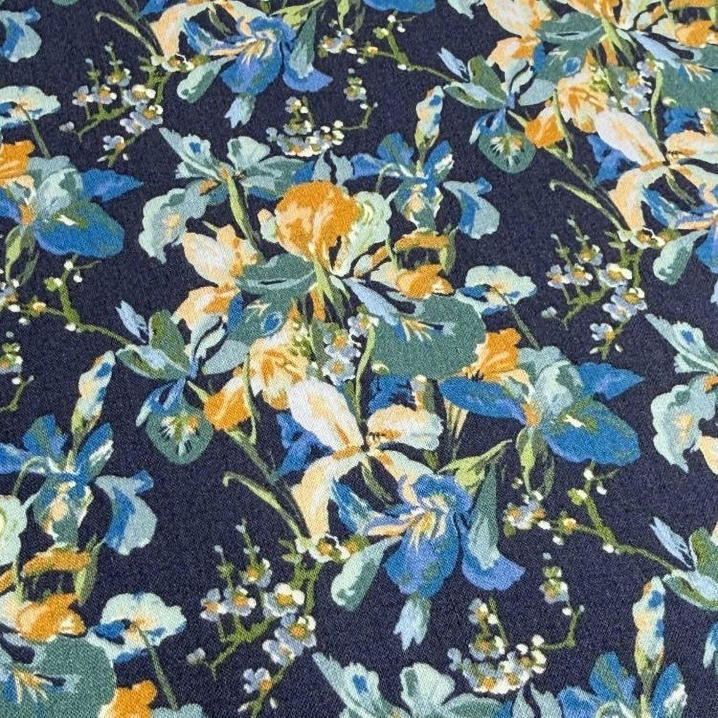 The image is a close-up view of a fabric with a floral pattern in shades of blue, green, and yellow. The pattern consists of various flowers and leaves, creating a vibrant and colorful design.