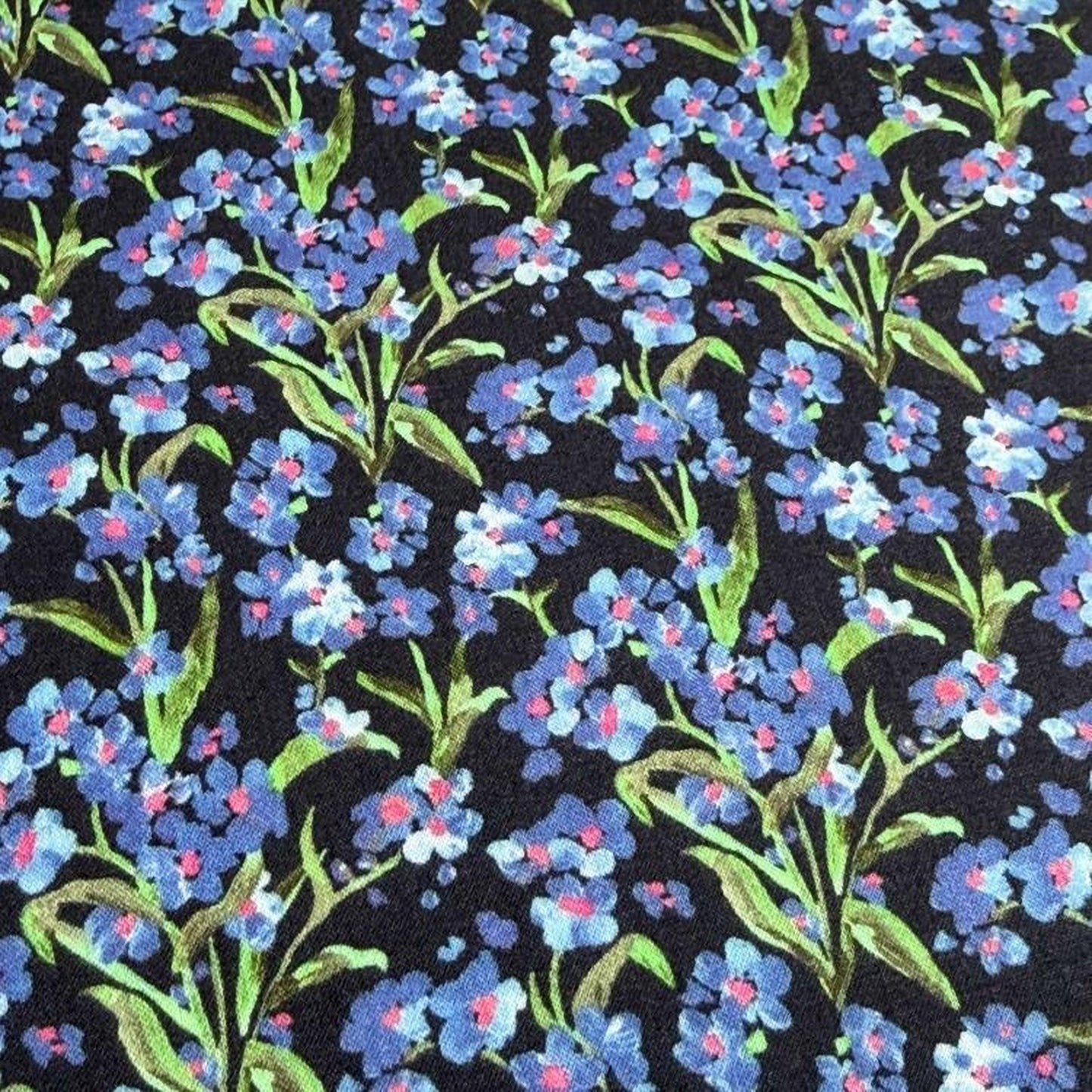 a close-up view of a fabric with a floral pattern. The fabric is predominantly black, with blue and white flowers scattered across it. The flowers appear to be in full bloom, creating a vibrant and lively visual effect. The pattern repeats itself throughout the fabric, creating a sense of continuity and rhythm.