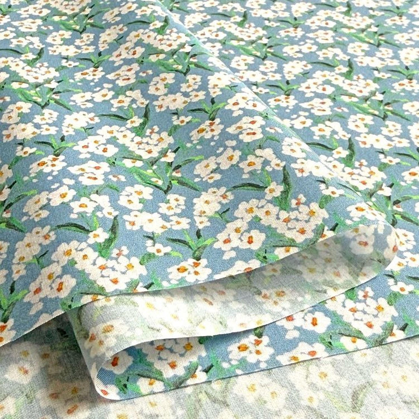a close-up view of a fabric with a floral pattern, featuring white flowers with green leaves. The fabric appears to be folded or rolled, revealing the intricate design of the flowers.