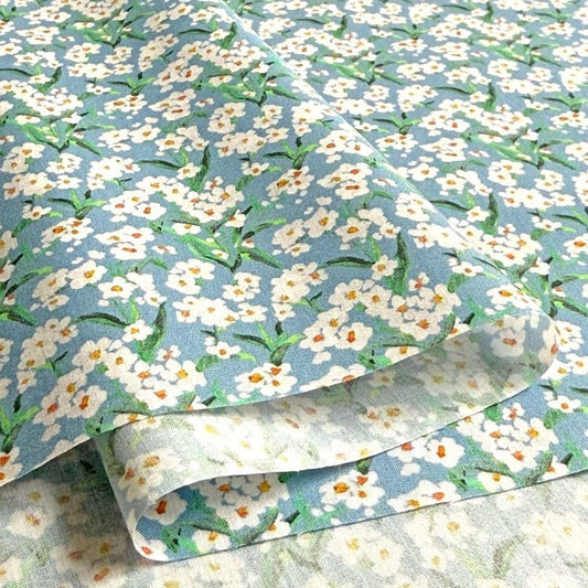 a close-up view of a fabric with a floral pattern, featuring white flowers with green leaves. The fabric appears to be folded or rolled, revealing the intricate design of the flowers.