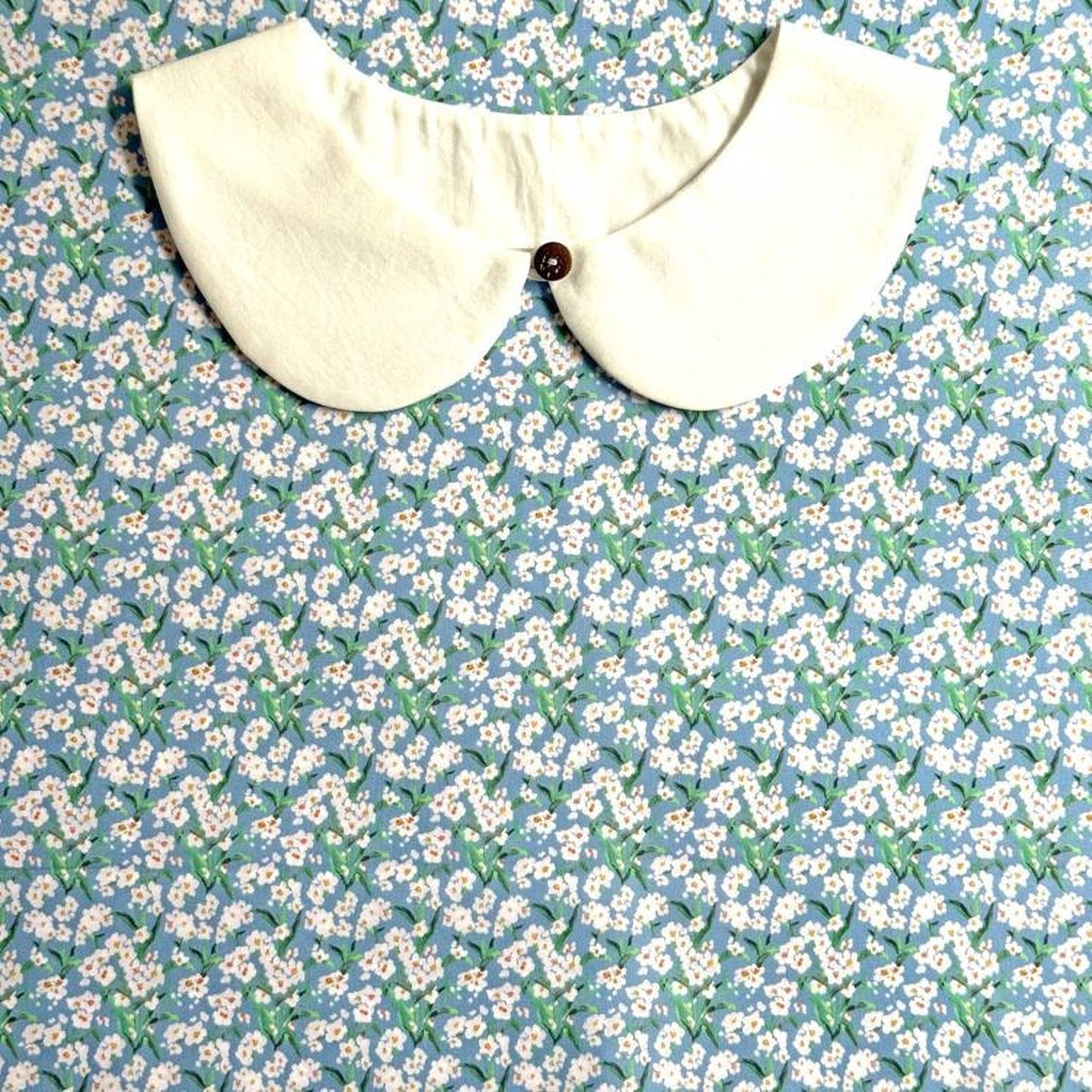 A white collar is displayed against a blue floral background.