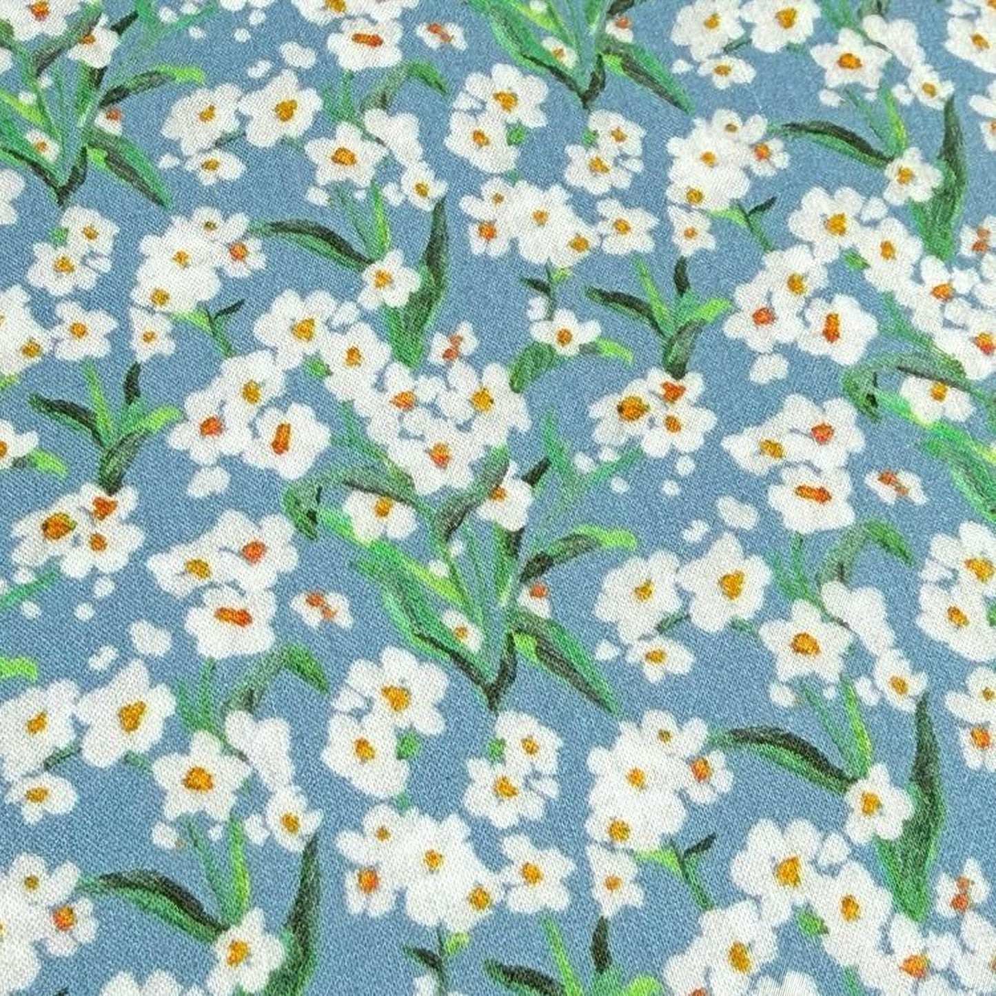 a close-up view of a fabric with a repeating pattern of white flowers with green leaves against a blue background.