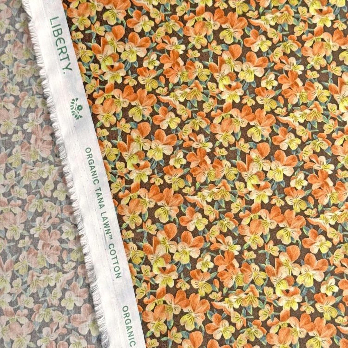 a close-up view of a fabric with a floral pattern, including orange and yellow flowers. The fabric appears to be made of cotton and is displayed on a white fabric ruler.
