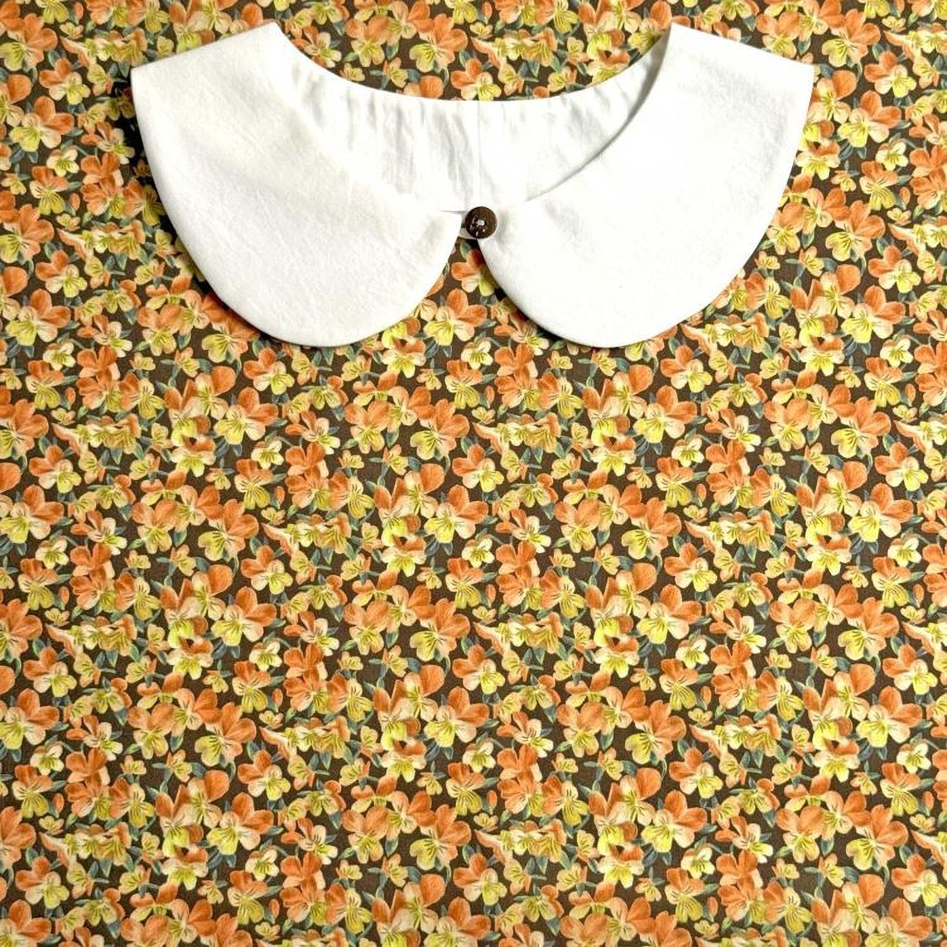 a white collar with a button, set against a background of a floral print with orange and yellow flowers.