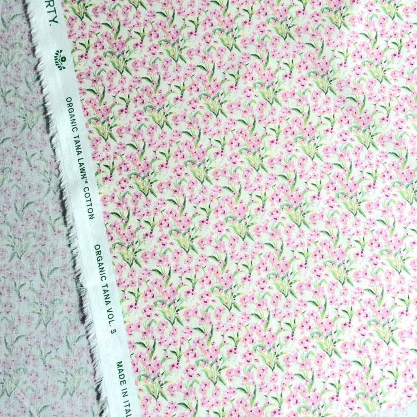 a close-up view of a fabric with a floral pattern in shades of pink and green. The fabric appears to be made of cotton and has a white label with text on it.