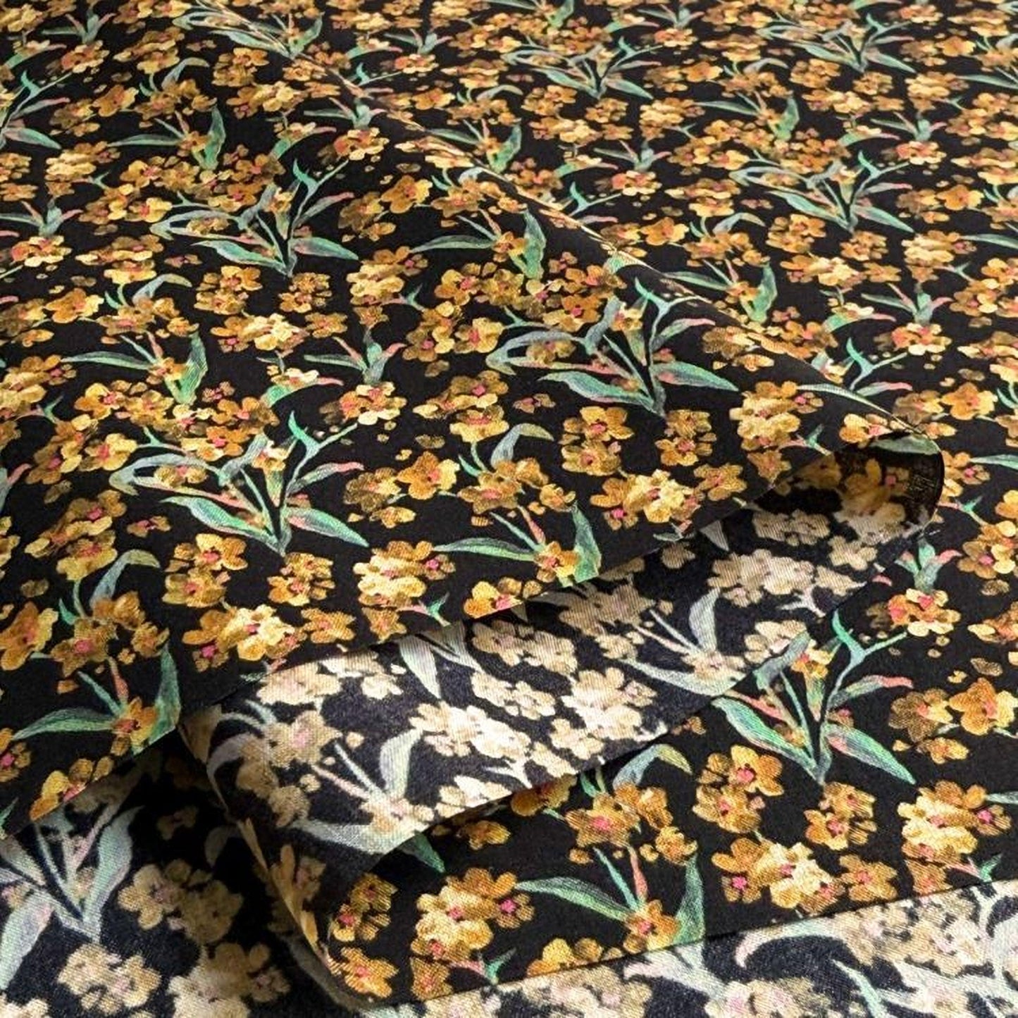 a close-up view of a fabric with a floral pattern in shades of yellow and black. The pattern consists of numerous small flowers and leaves, creating a visually striking and intricate design. The fabric appears to be a piece of clothing or textile, with the floral pattern covering the entire surface.