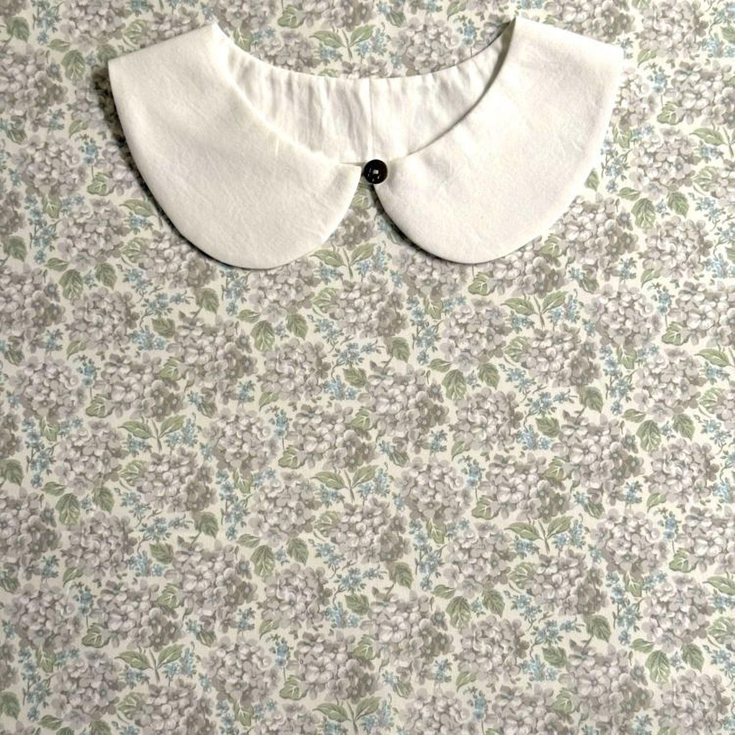 A white collar with a button is displayed on a floral print fabric background.