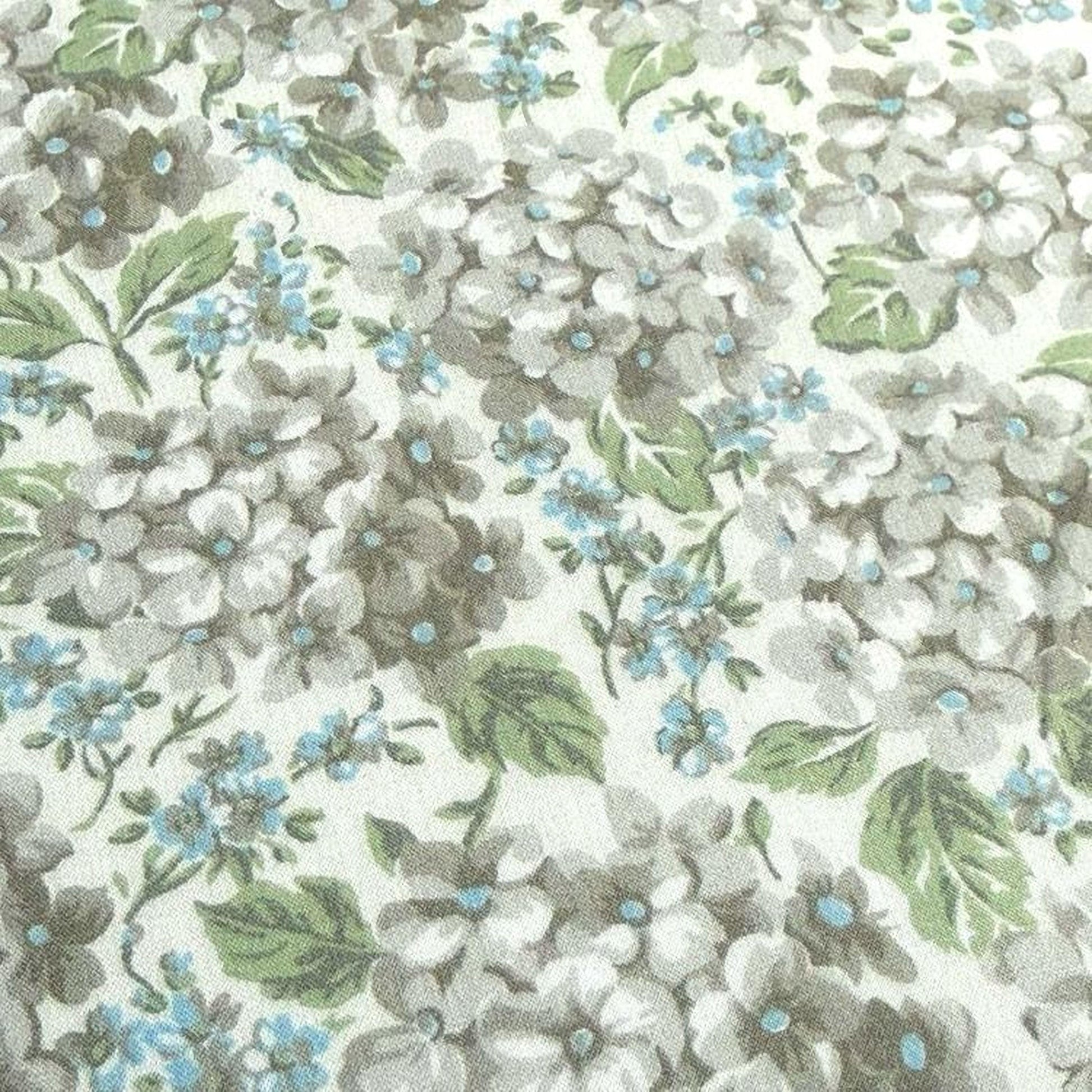 a close-up view of a fabric with a floral pattern. The pattern consists of various shades of green and white flowers, interspersed with green leaves. The flowers are arranged in a way that creates a sense of depth and texture, with some flowers appearing larger and more detailed than others. The overall composition of the image is visually appealing and showcases the intricate details of the floral pattern.