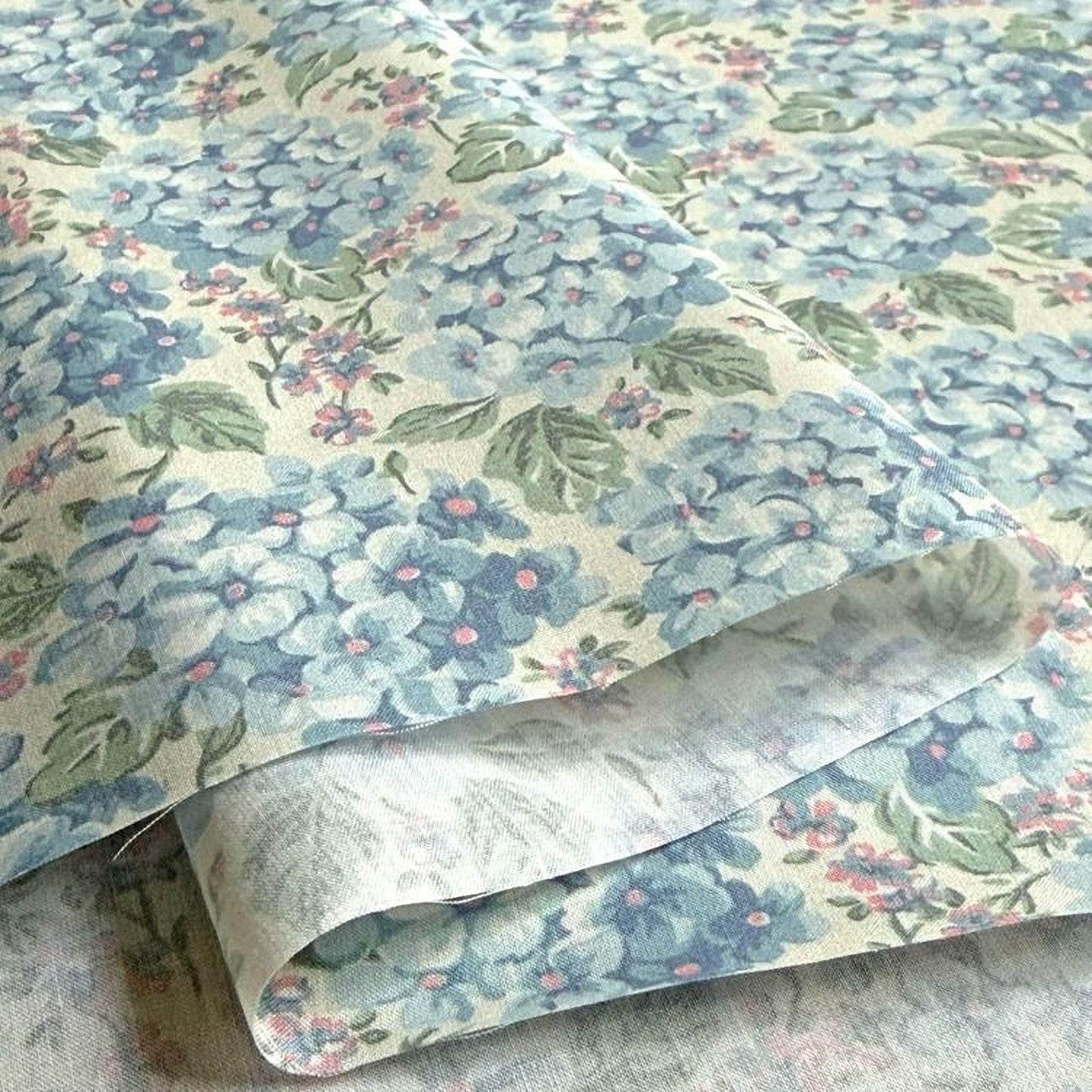 a close-up view of a fabric with a floral pattern in shades of blue and green. The fabric appears to be folded or rolled, revealing the intricate design of the flowers and leaves.
